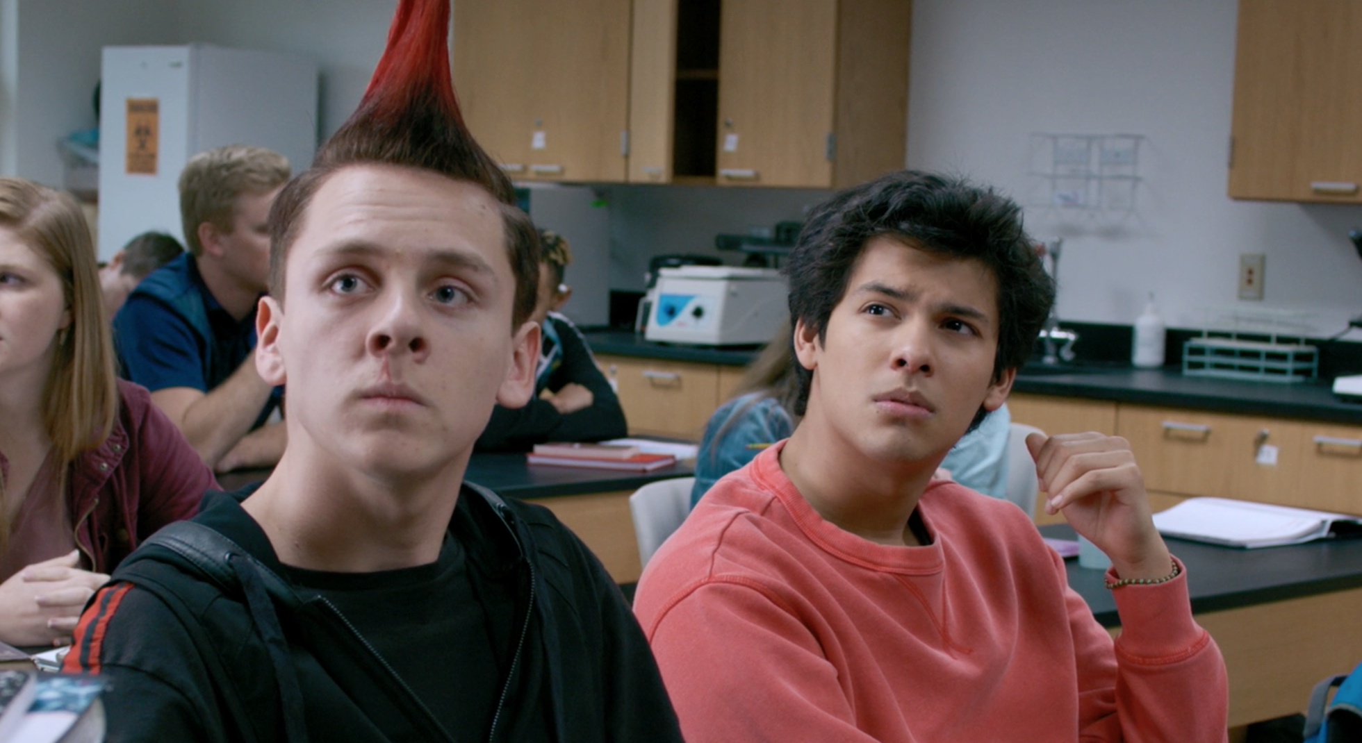 Hawk and Miguel from Cobra Kai (TV show) sit in a school classroom looking to the side. 