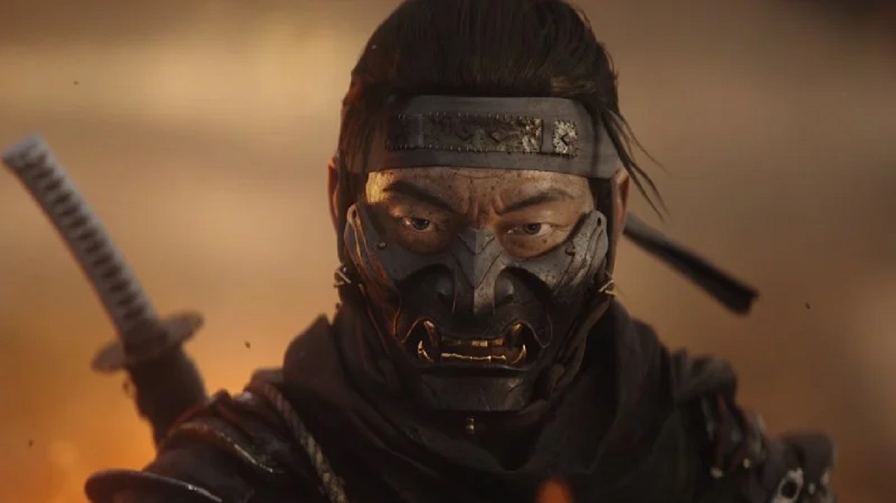 Jin Sakai stares forward into the camera. He is wearing the mask and headband of the Ghost of Tsushima. The hilt of his sword can be seen over his right shoulder.