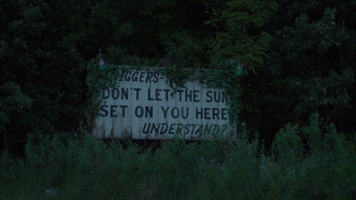 A billboard reads, "Niggers Don't Let the Sun Set on You Here, Understand?" 