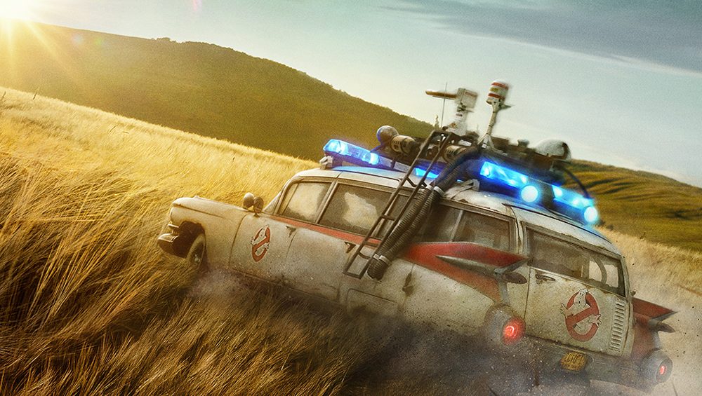 An old car with scientific equipment attached to the roof drives through a field of tall grass.