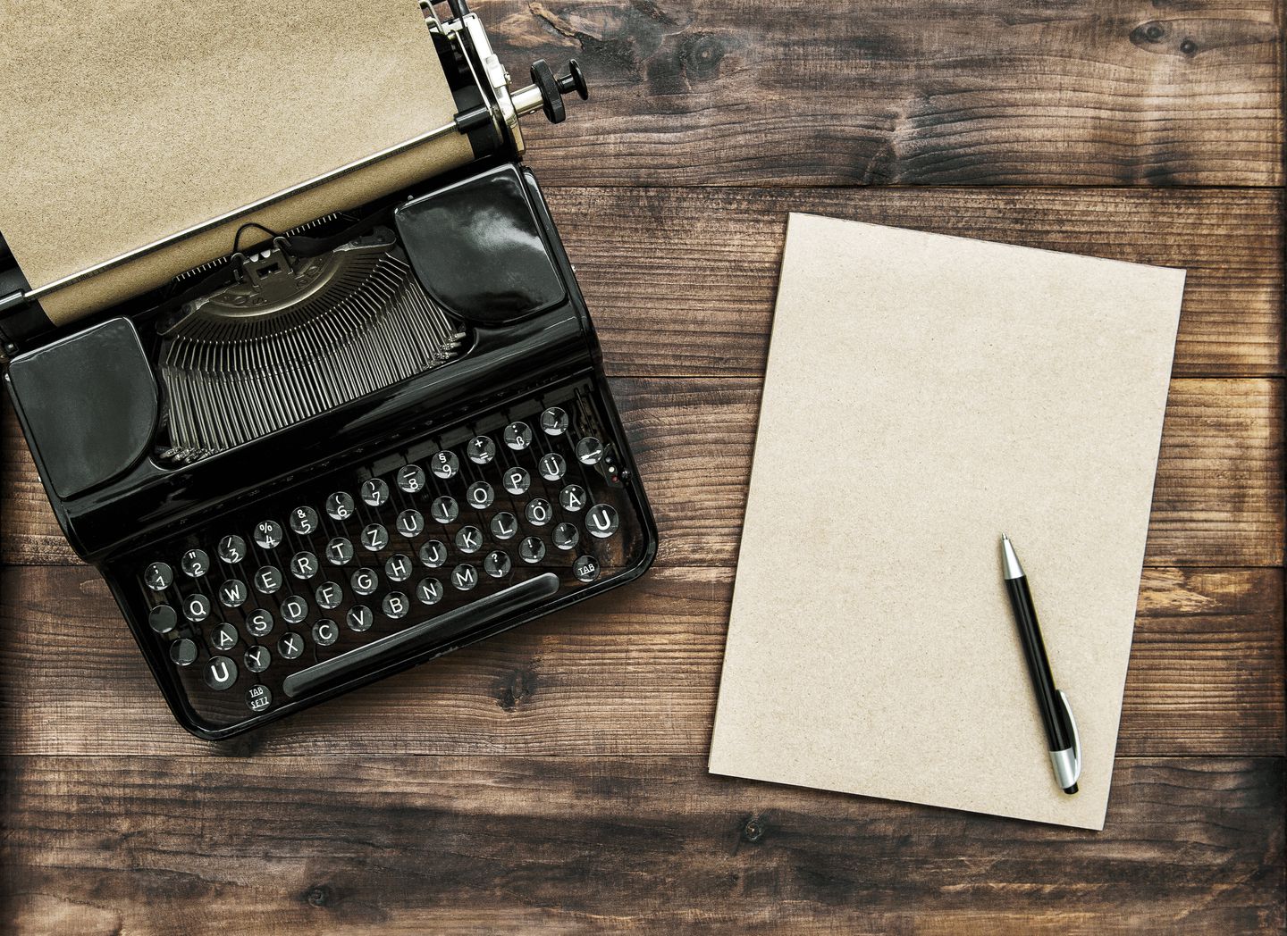 Supplies for writing fanfiction, a typewriter, notepad, and pen, sit on a table.