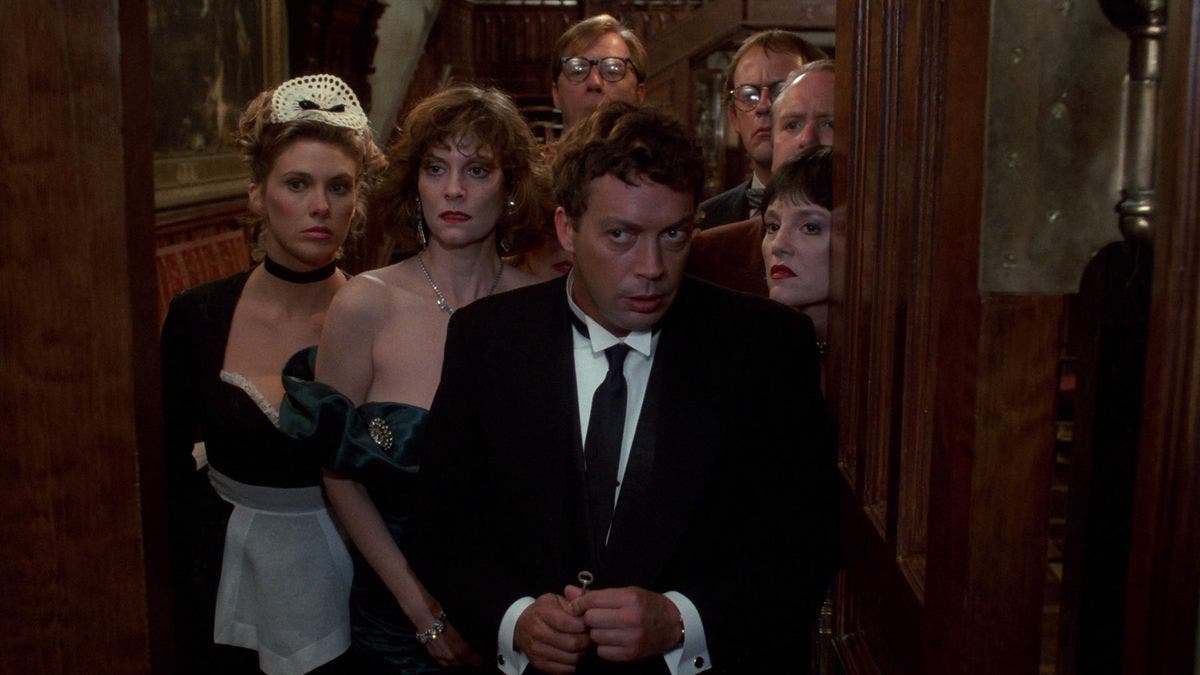 The cast of Clue stands outside the mansion, looking into the camera.