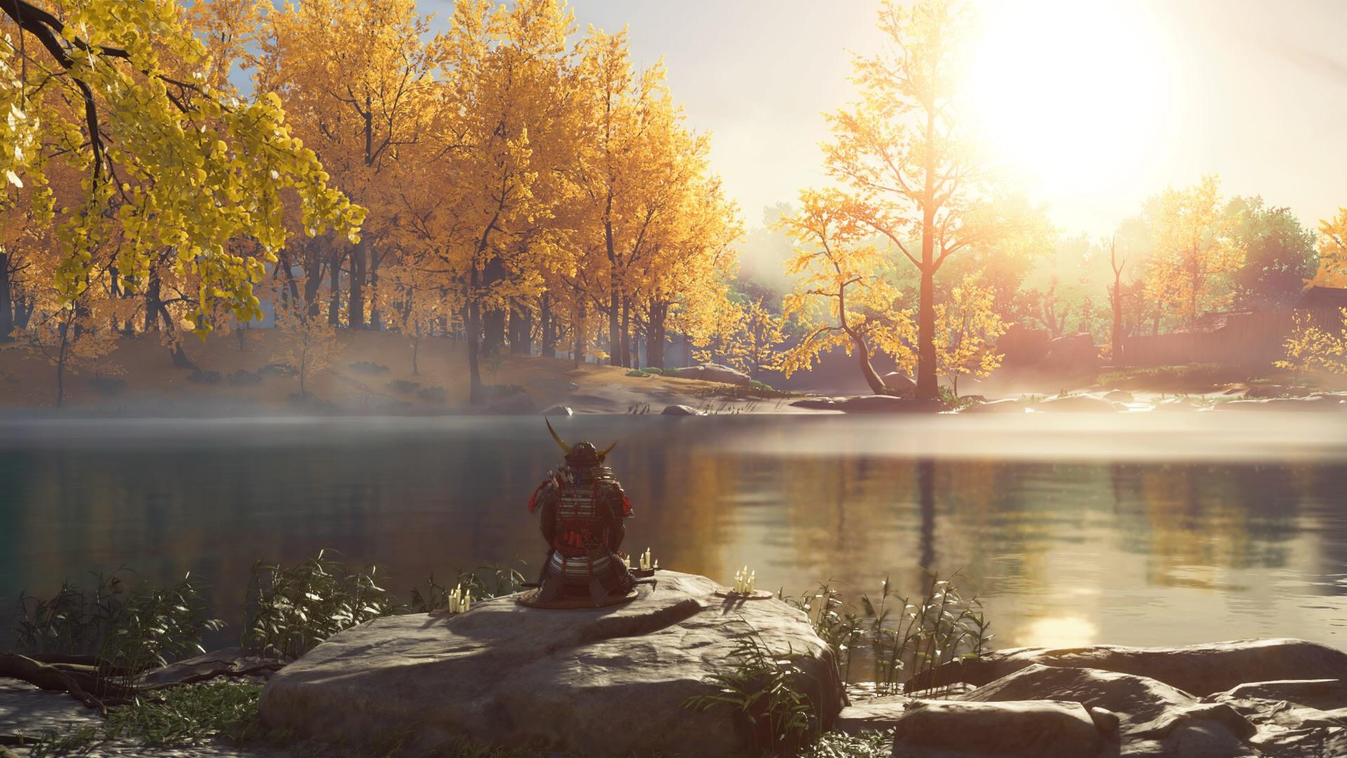 Jin Sakai, the protagonist of "Ghost of Tsushima," sits with his back turned to the viewer in front of a still lake. Across the lake is a forest of trees with golden leaves.