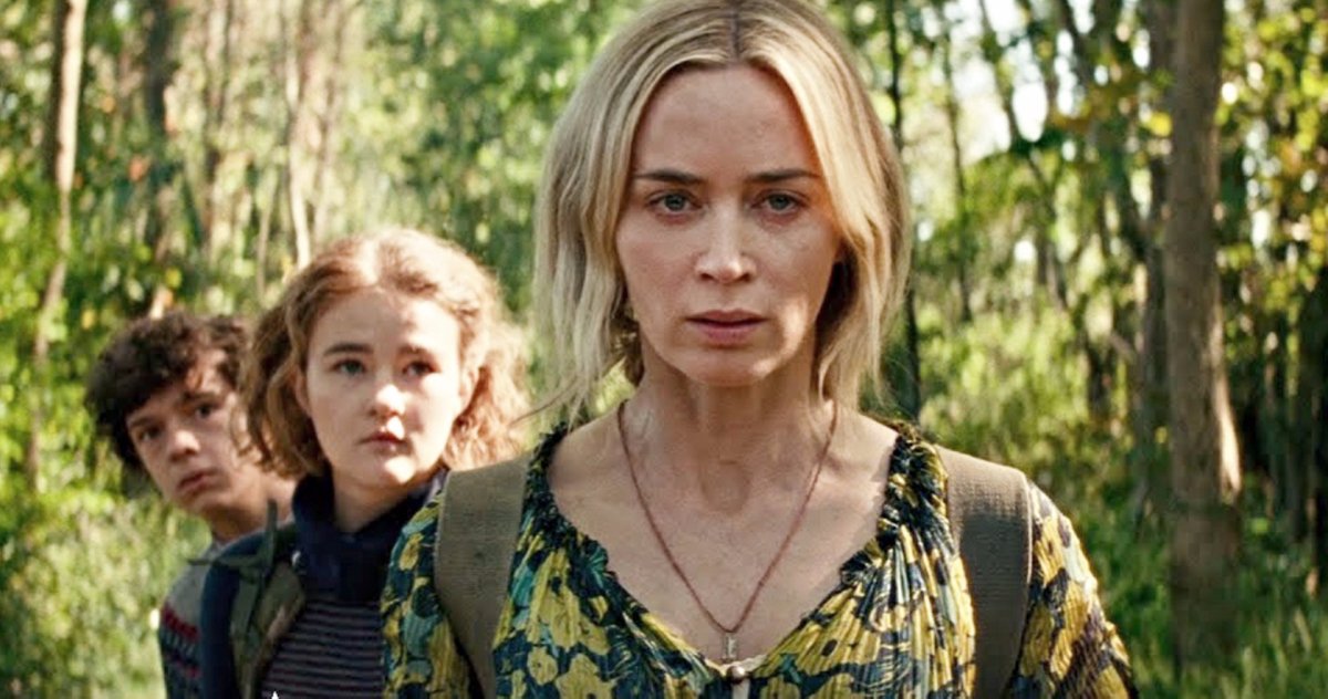 A woman and her two children stand in a line, gazing at the camera. in the background is a forest of trees.