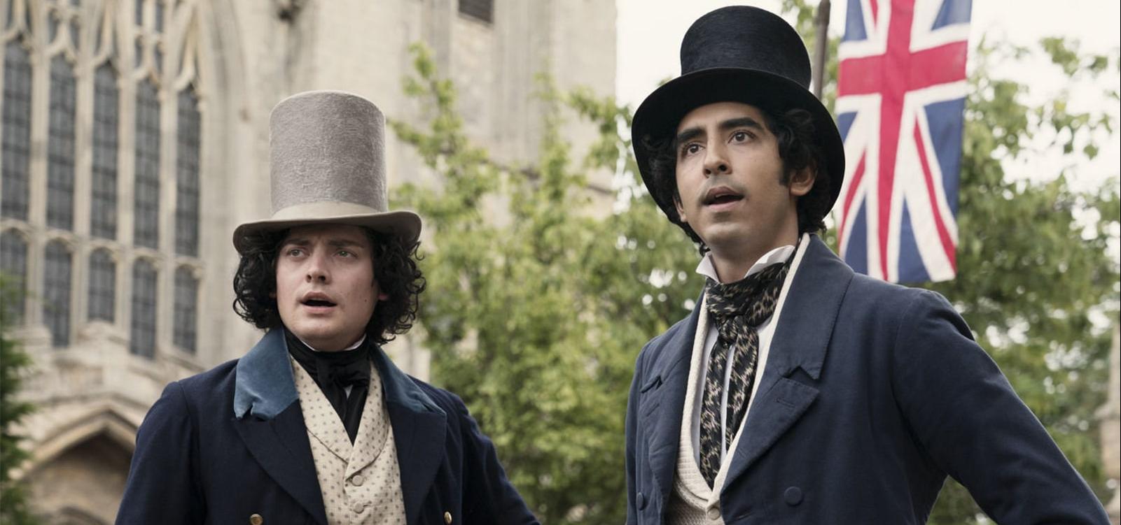 Two men in suits and top hats gaze at something off-screen. In the background is a Union Flag and a large building.