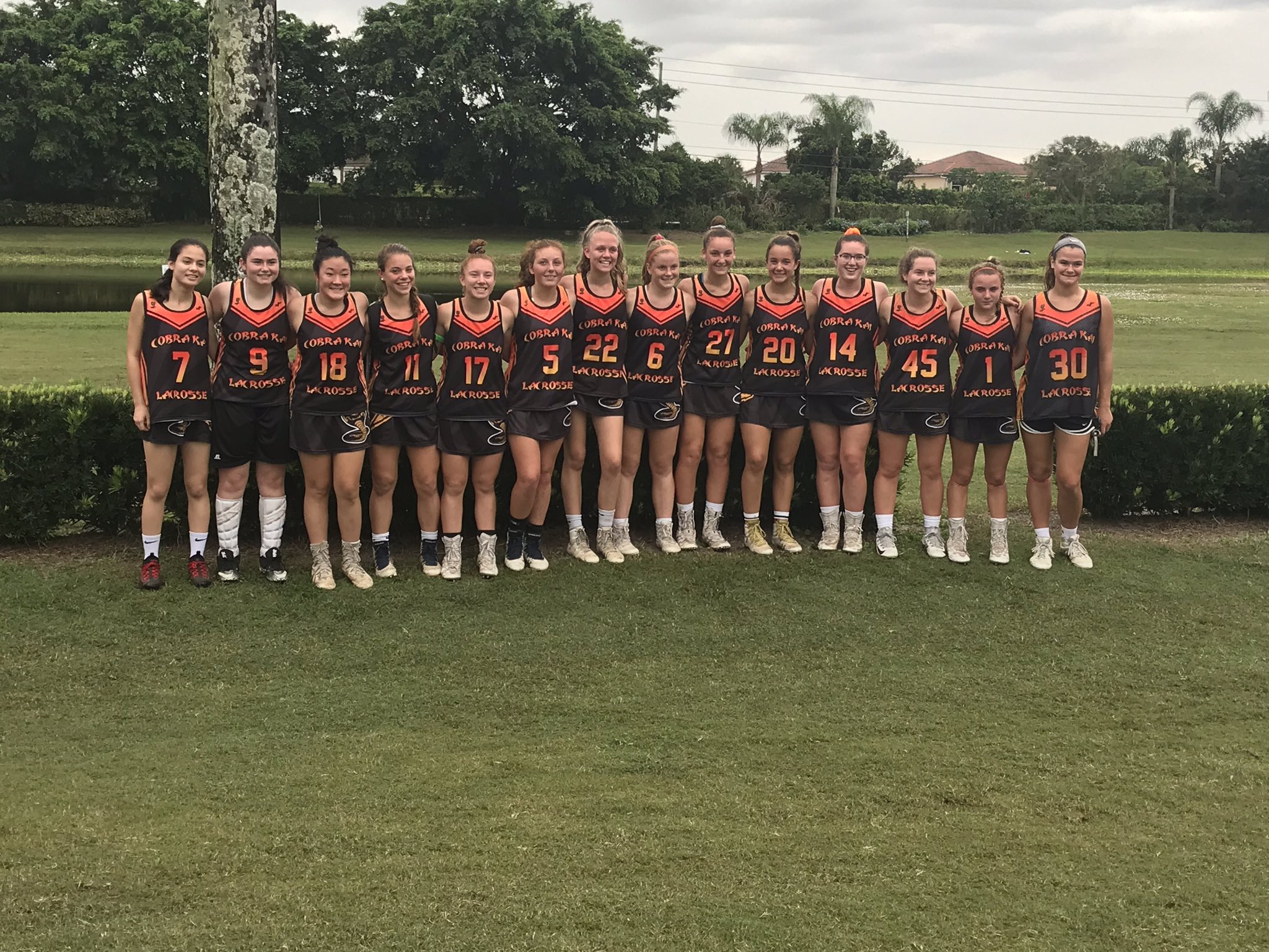 2021 Cobra Kai Lacrosse team dressed in black uniforms stand in a row on a green lawn in Florida.