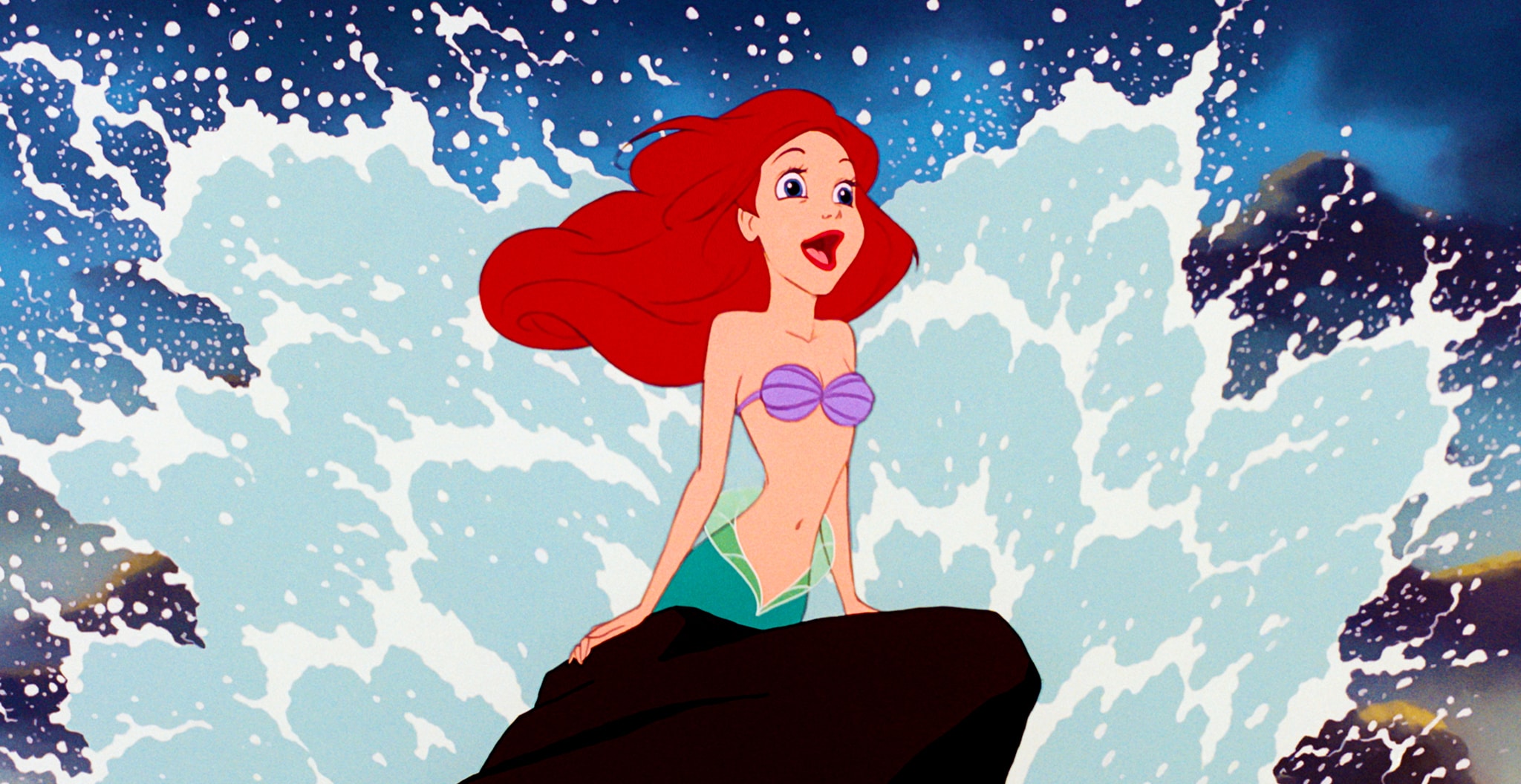 Ariel leans against a rock with a wave splashing behind her.
