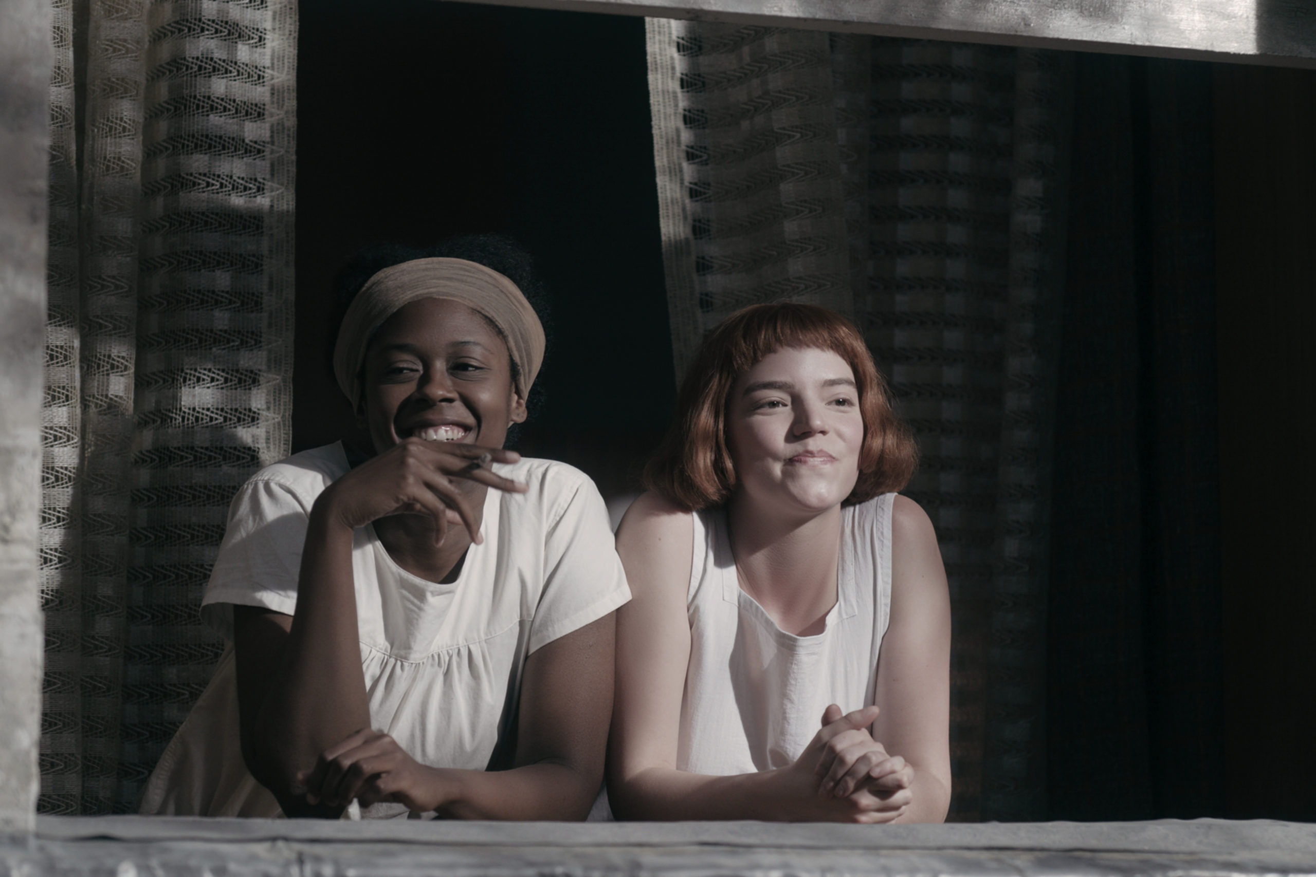 Jolene (Moses Ingram) and Beth Harmon (Anya Taylor-Joy) lean over the window sill to overlook the front yard of their orphanage dressed in white pajamas.