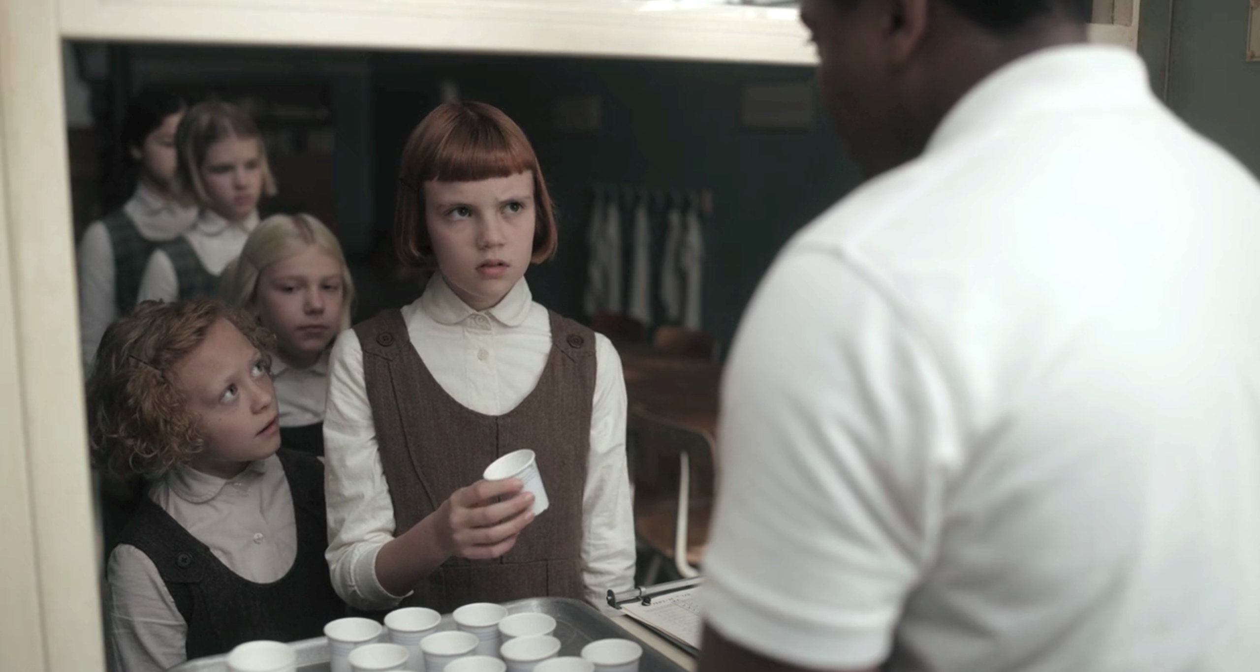 Young Beth Harmon (Isla Johnston) is waiting in line to receive her daily pill dosage from one of the orphanage's staff members.