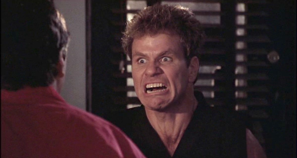 John Kreese screams at man in red shirt. 