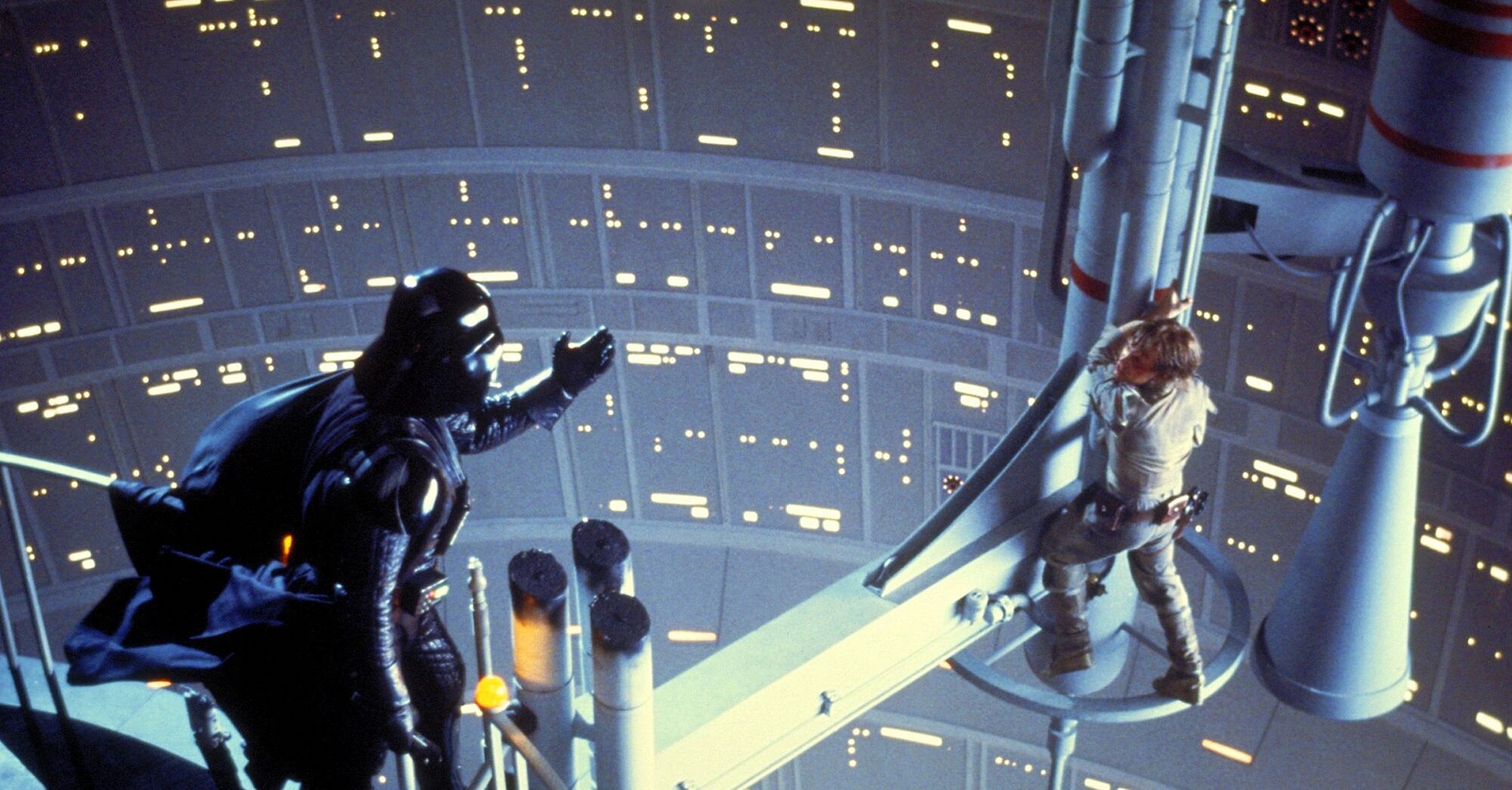 Darth Vader stares down Luke Skywalker, who is hanging precariously on a jutting piece of spaceship architecture.  