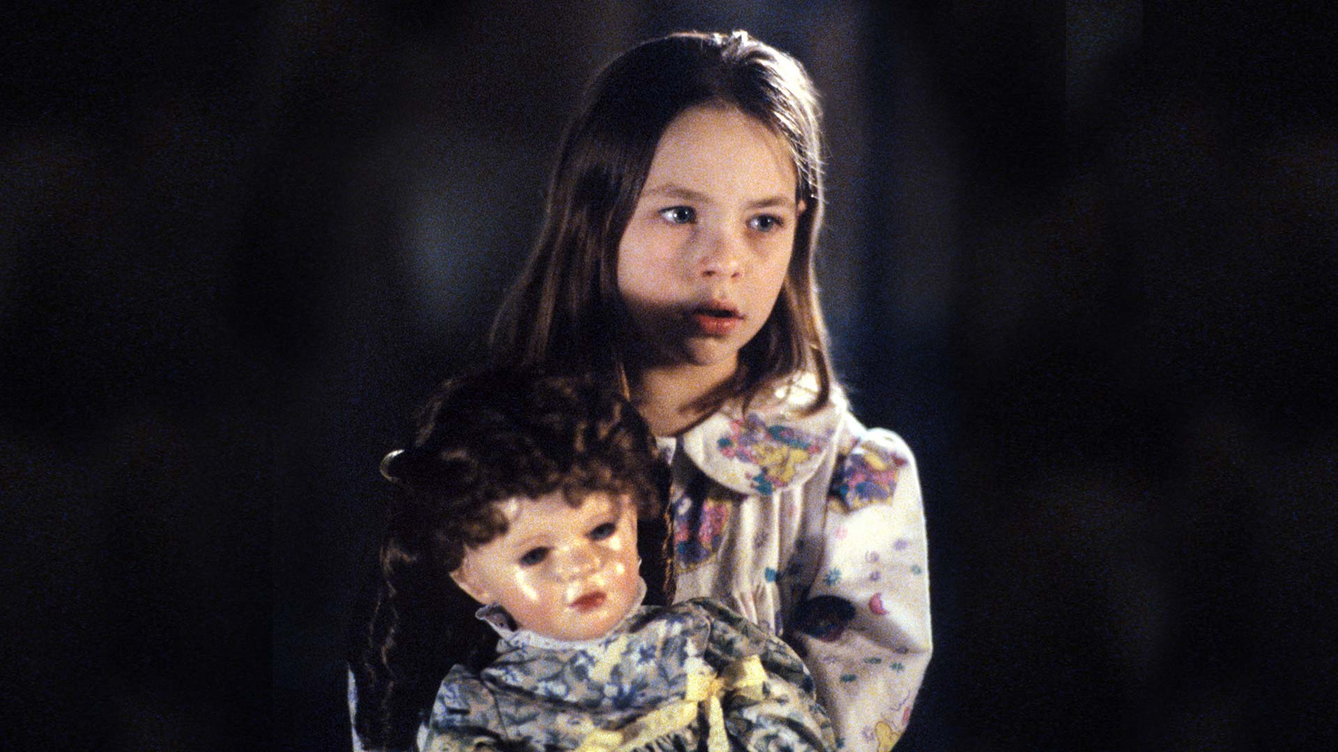 A young girl in pajamas holds a porcelain doll.