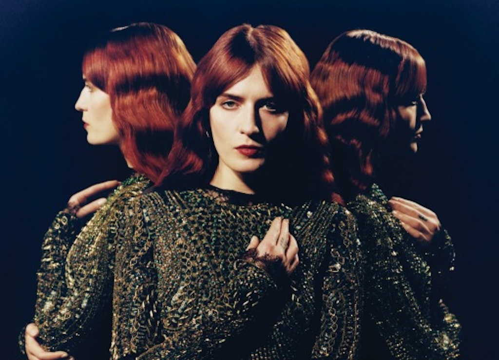 Florence Welch stands in the center with two reflections of herself to her left and right.