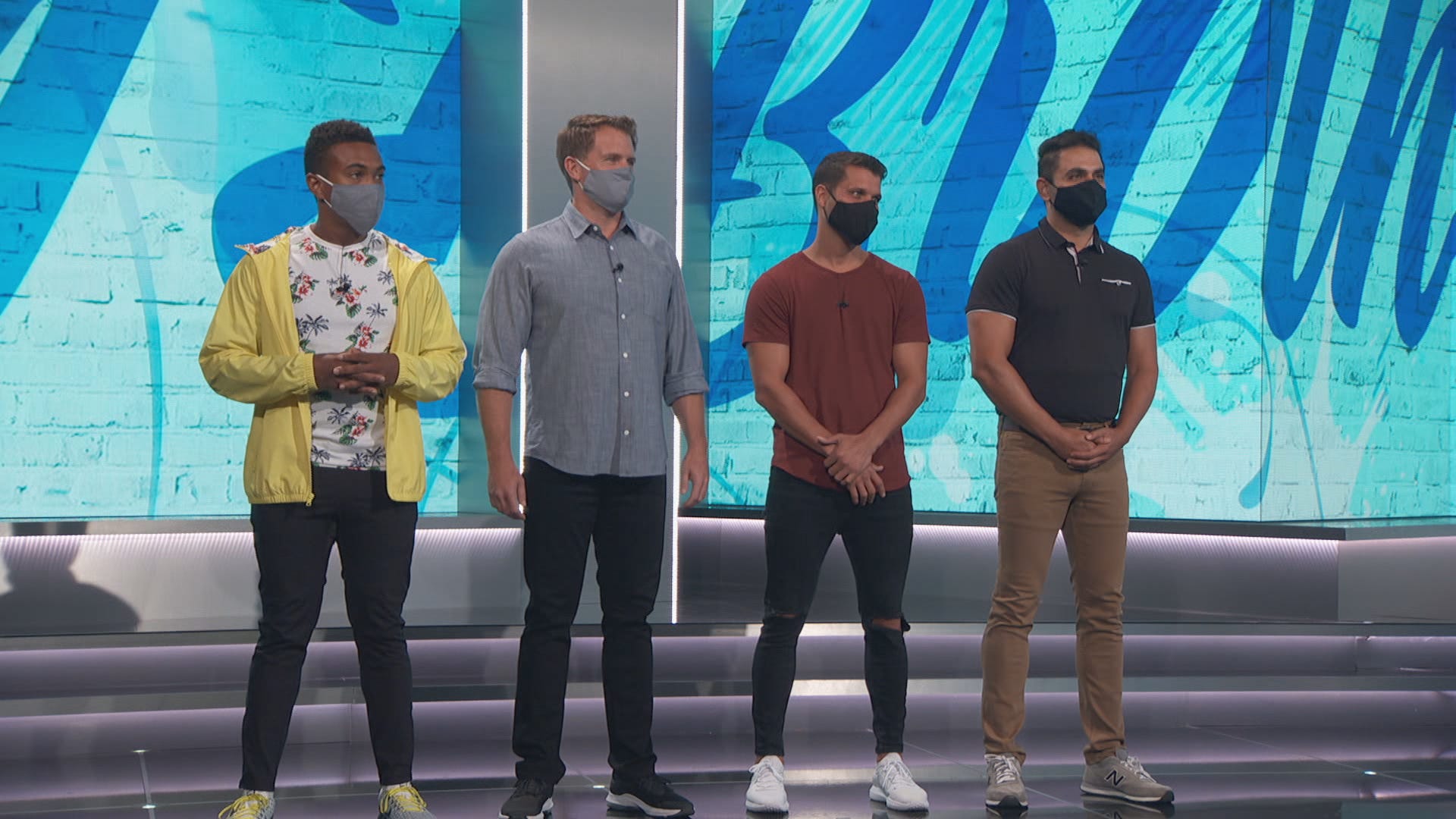 Contestants on Big Brother wear masks as they stand close together on set.