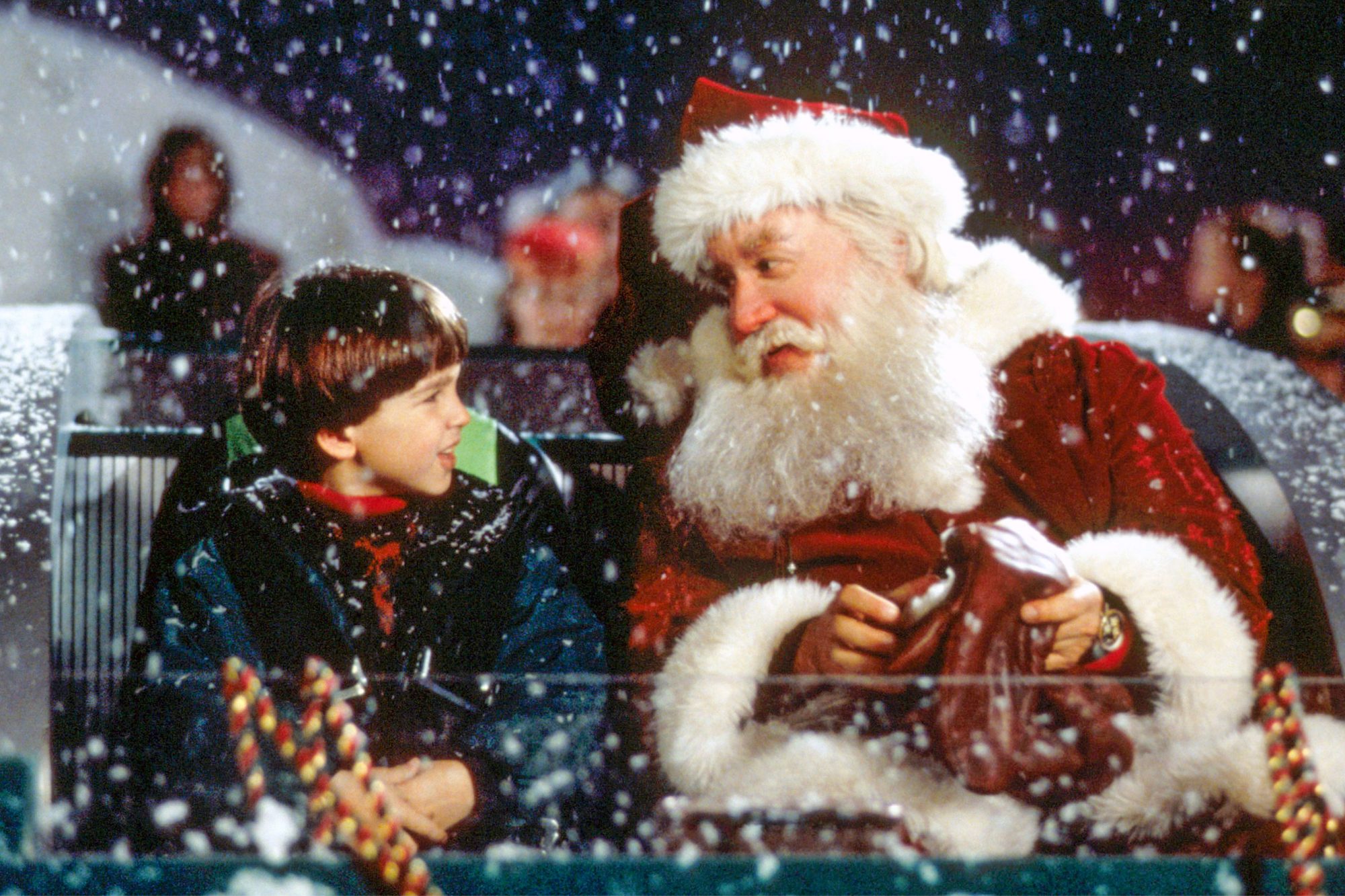 Santa Claus (aka Scott Calvin) sits in his sleigh with his son, Charlie, as snow falls around them.