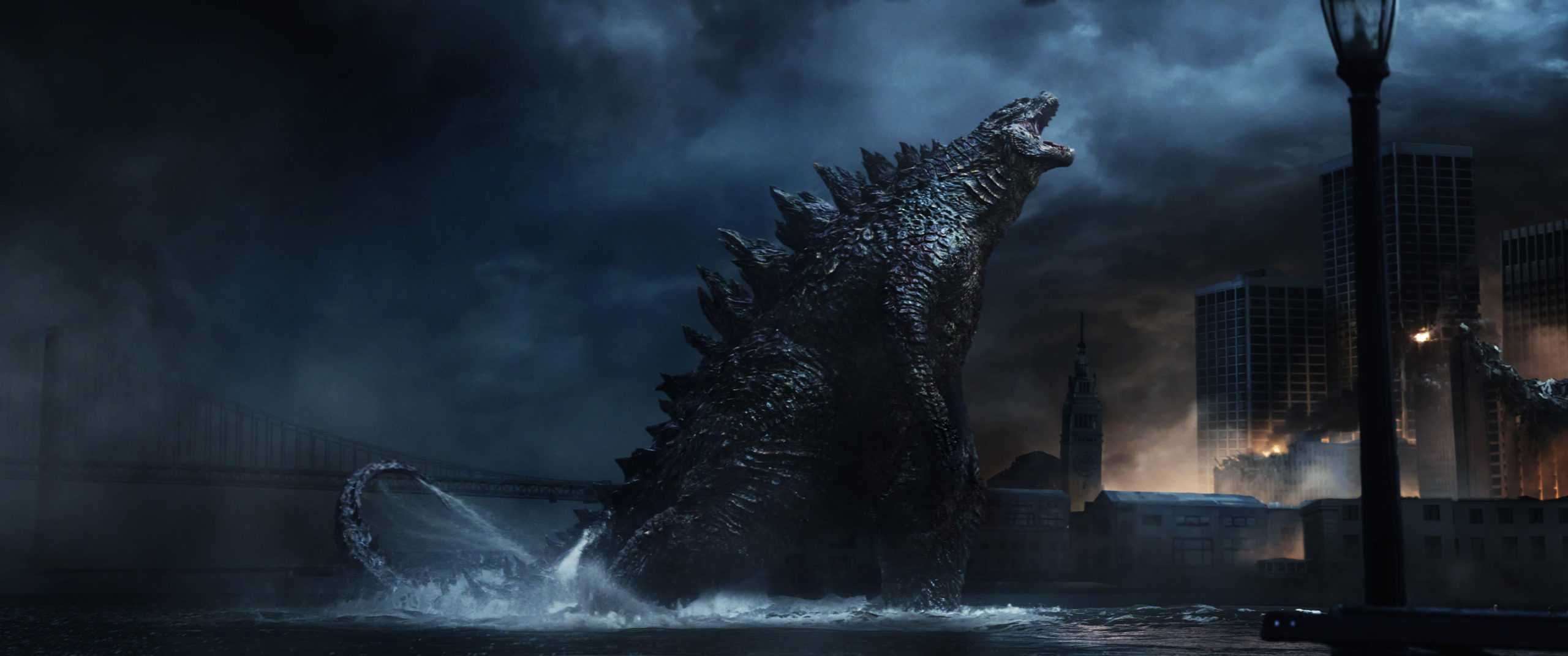 Godzilla standing in water and roaring towards the city.