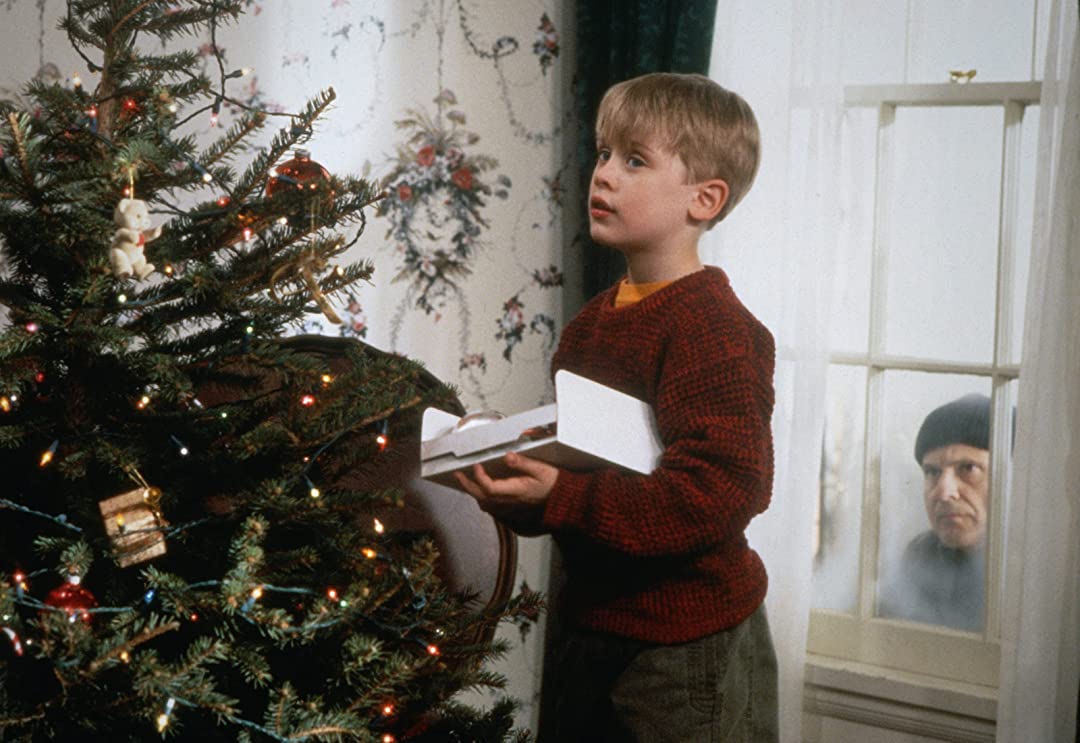 Kevin decorates the Christmas tree as a burglar looks on from outside the window.