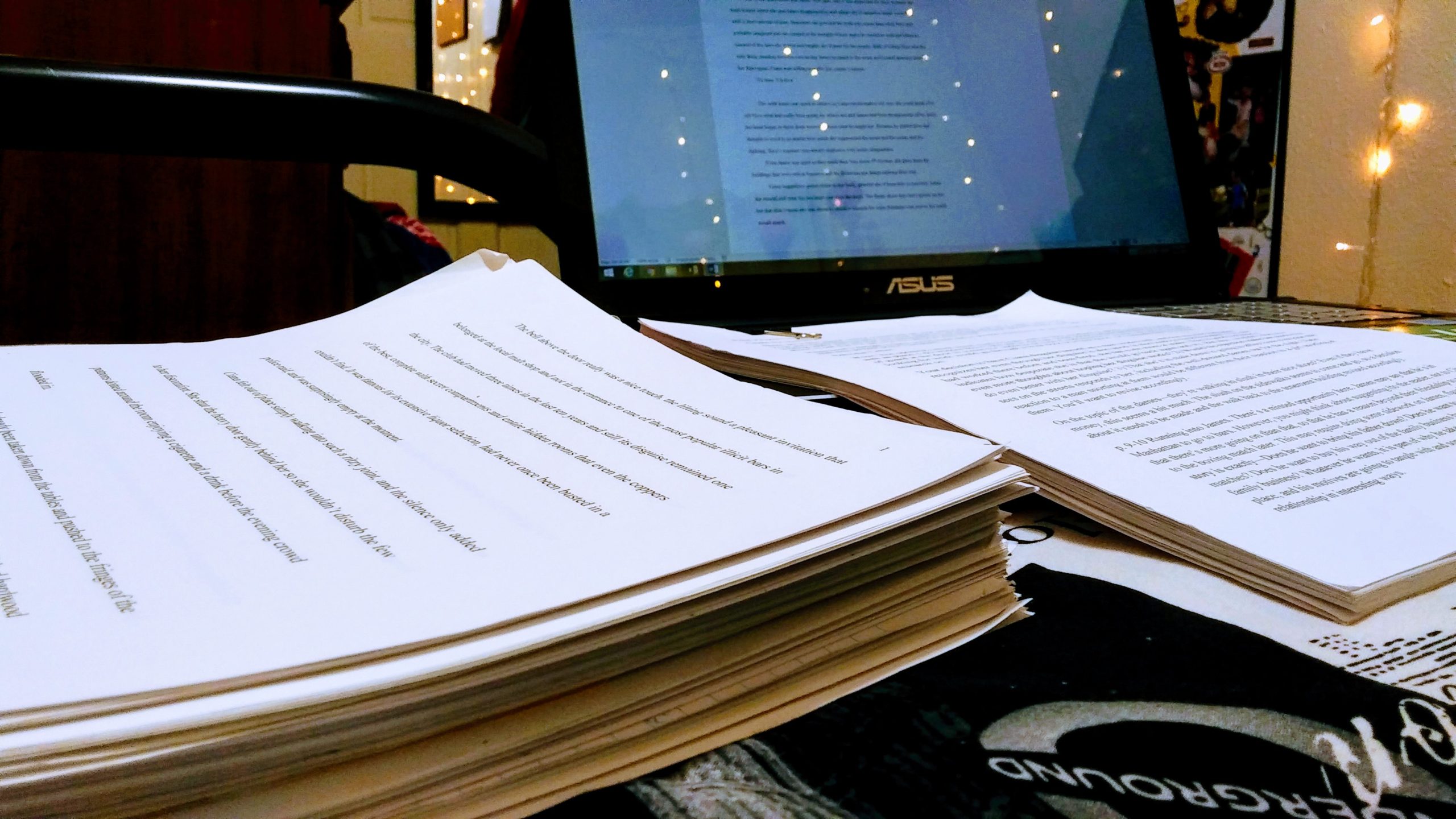 Stacks of paper from a manuscript sit in front of a laptop.