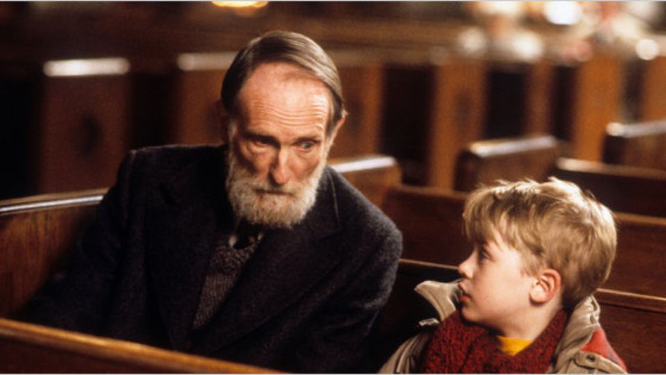 Kevin sits and talks with an old man, Marley, in a traditional church pew. 