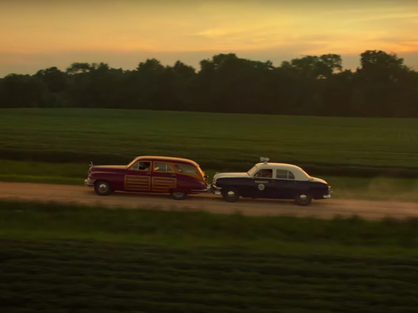 A police car tails the station wagon. 