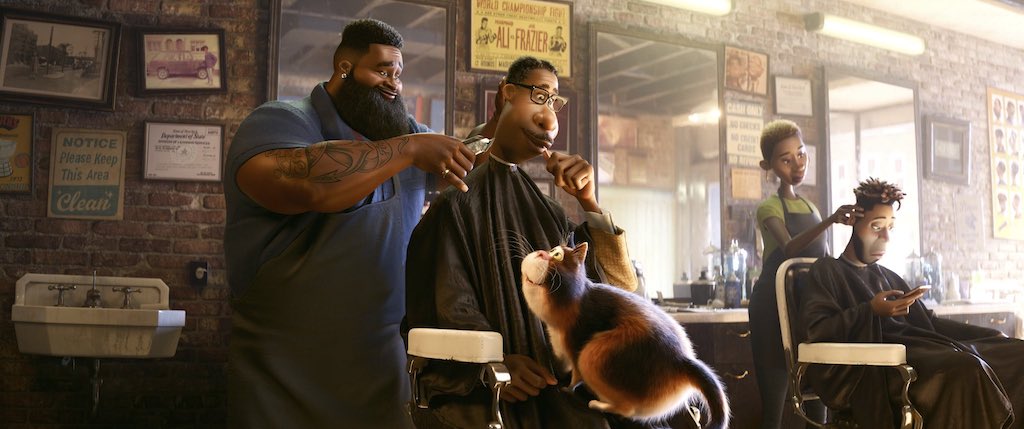 Joe sits in the barber chair with the cat on his lap as dev the barber cuts his hair.