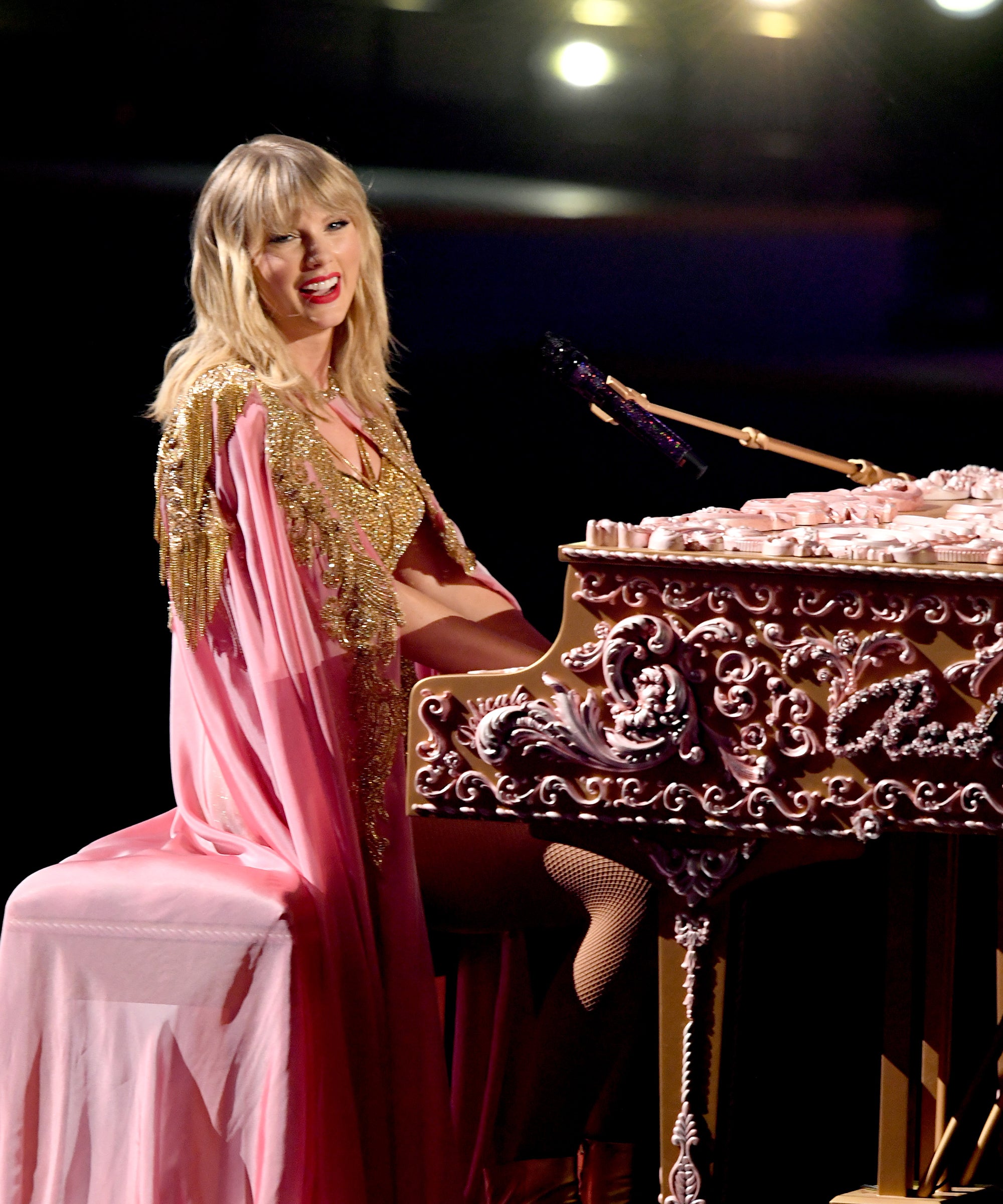 Taylor in a bedazzled pink costume at the piano during a show.