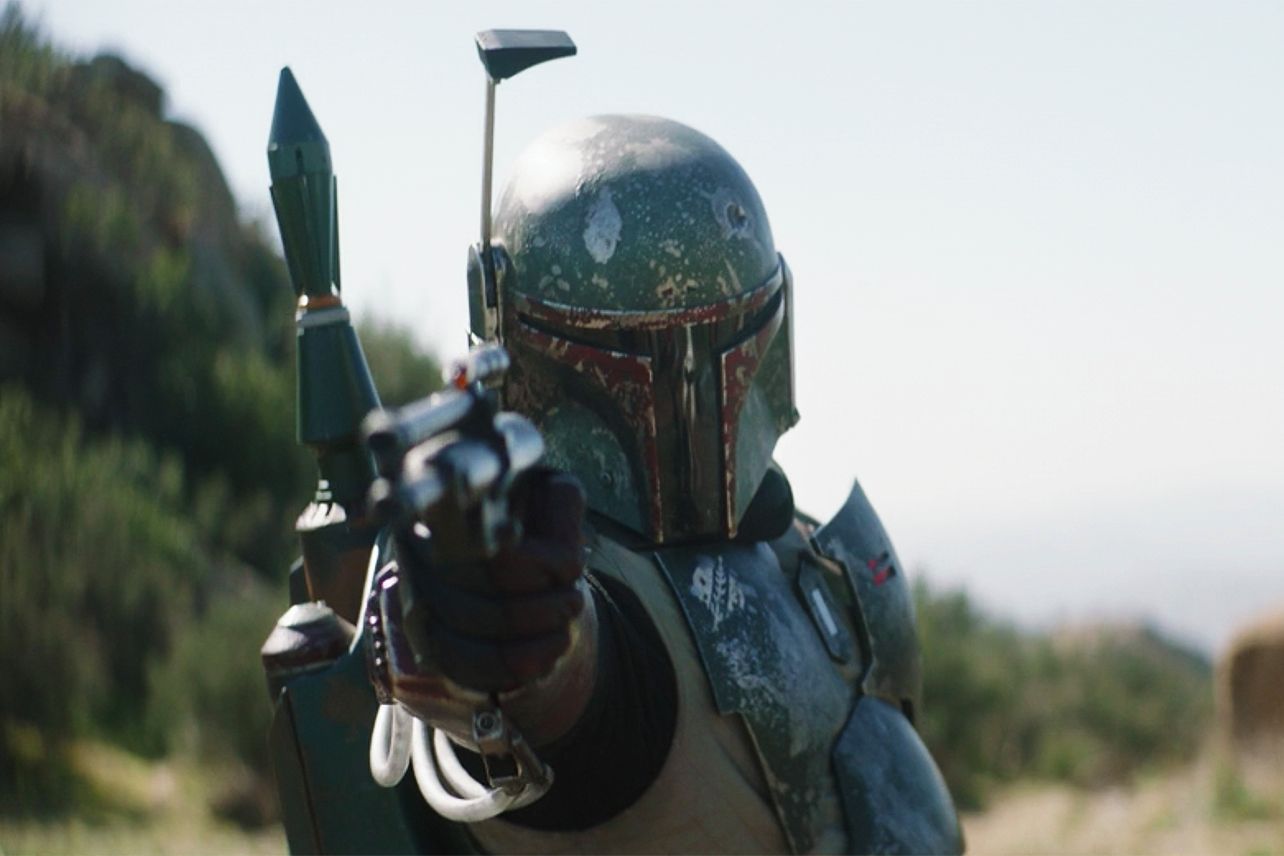 Boba Fett wears his scratched armor and holds out his blaster.