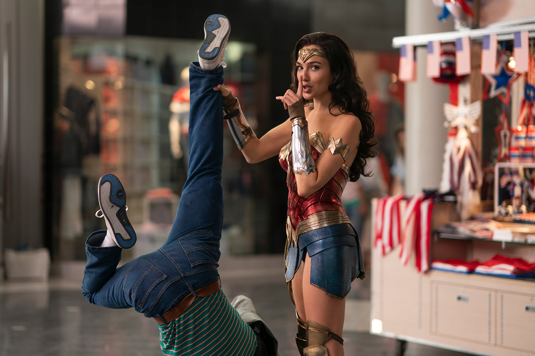 Wonder Woman stands in gold, red, and blue battle outfit, holding a man by his ankles. 