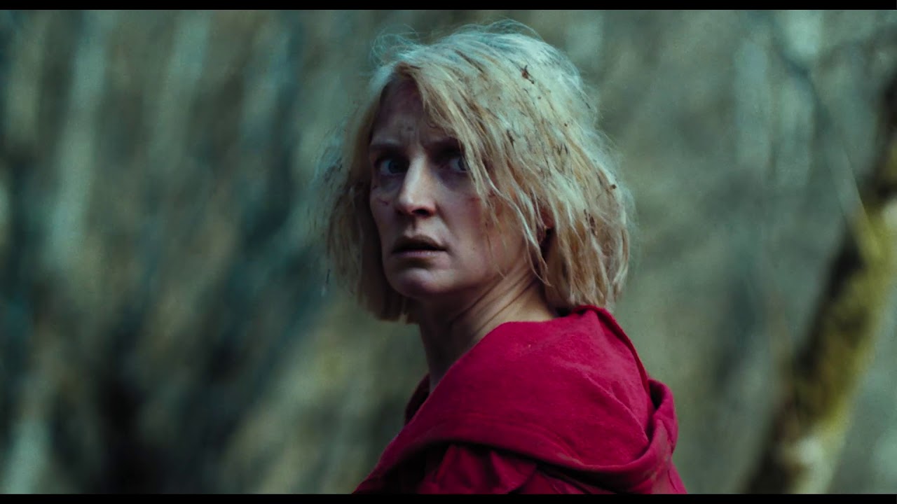 Woman standing in the woods with a red coat on. Paronnaud, Vincent. dir. Hunted, 2021.