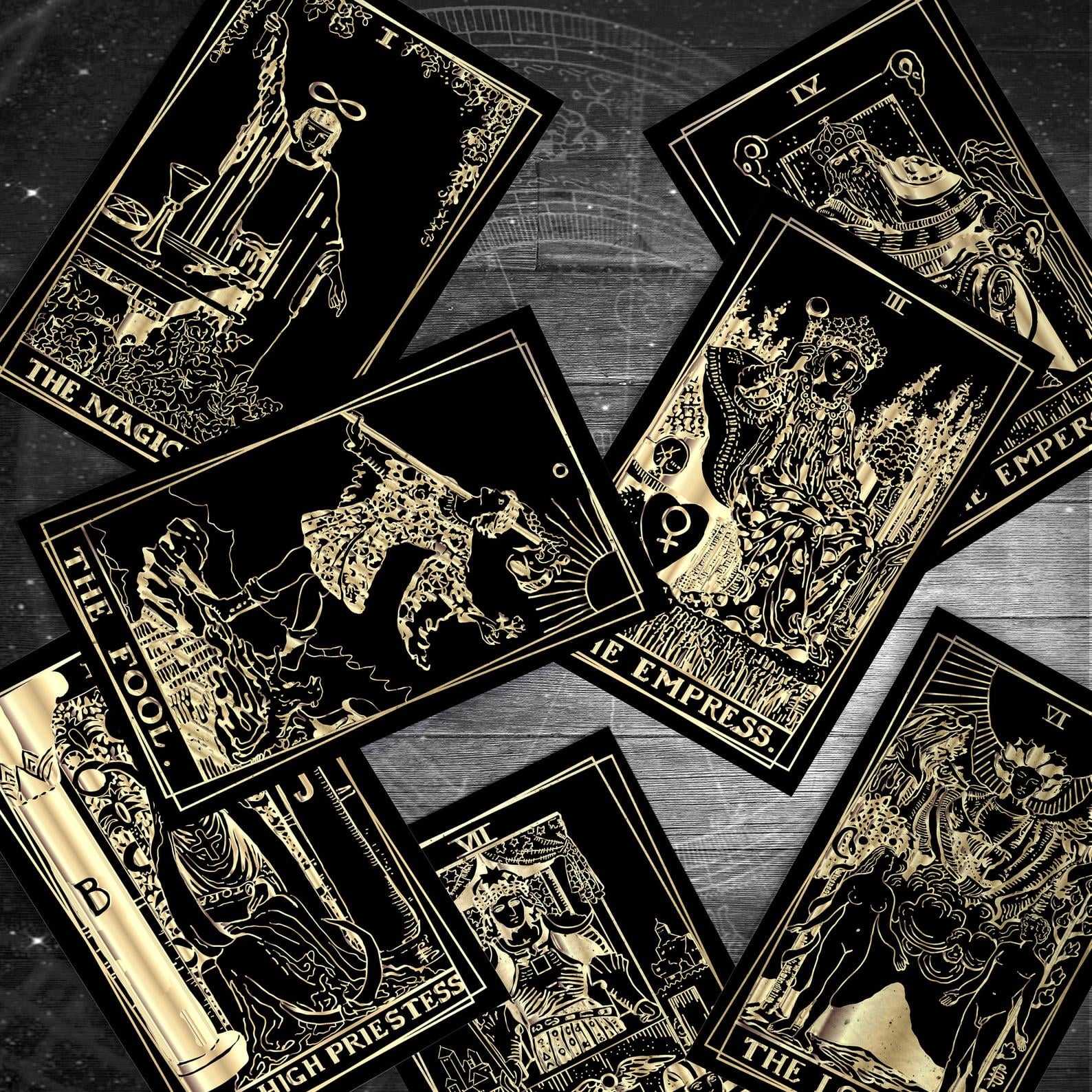 A black and gold tarot card set laying upon a grey wooden surface.