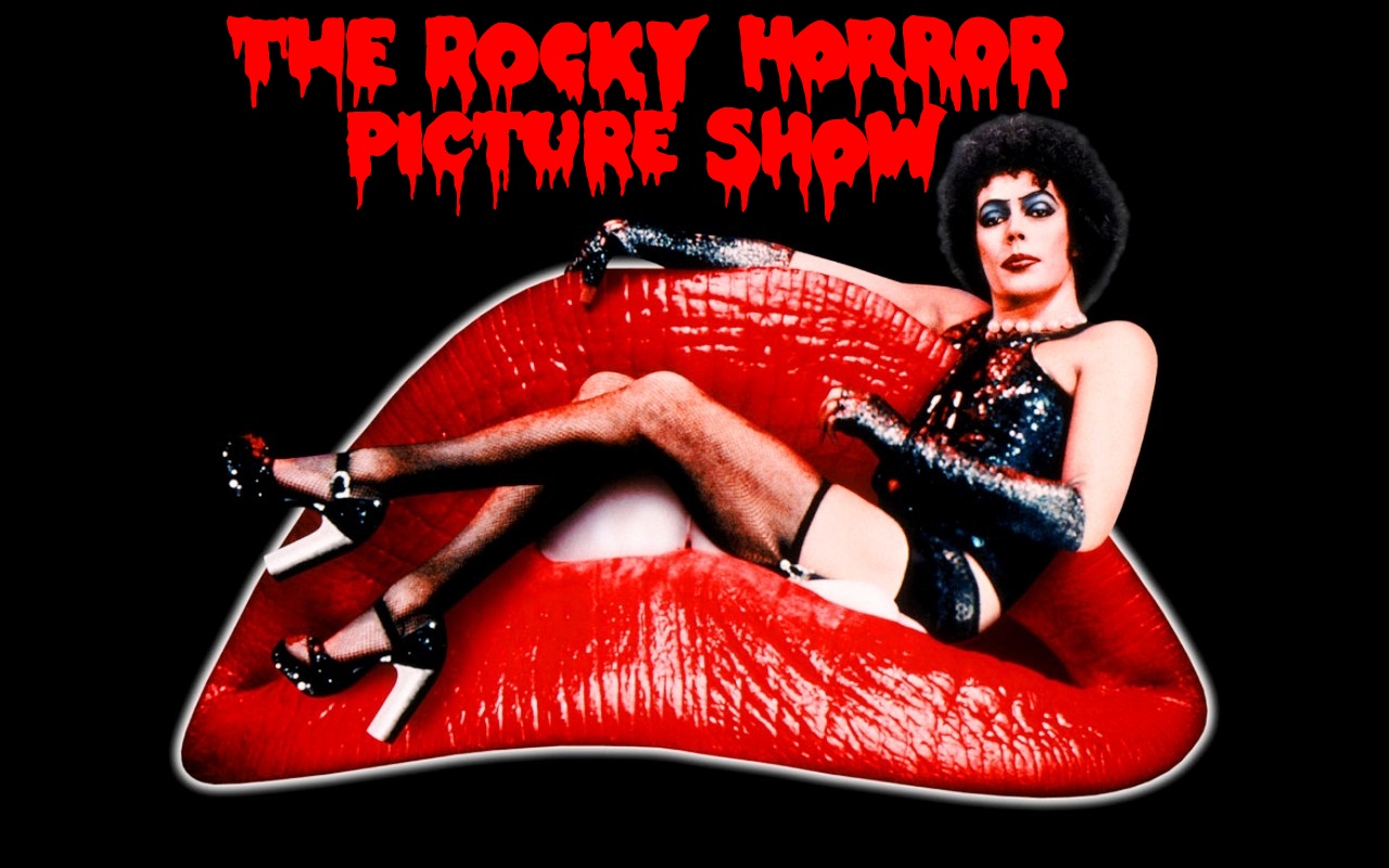 A Rocky Horror Picture Show Poster. The title of the movie is on top, in dripping red font. Underneath is a mouth with bright red lipstick on. Lounging in the teeth of the mouth is Dr. Frankenfurter, a white man with dark, curly hair and wearing a sparkly black corset, black panties, thigh-high fishnets, and black patent-leather heels. It is all on a black background.