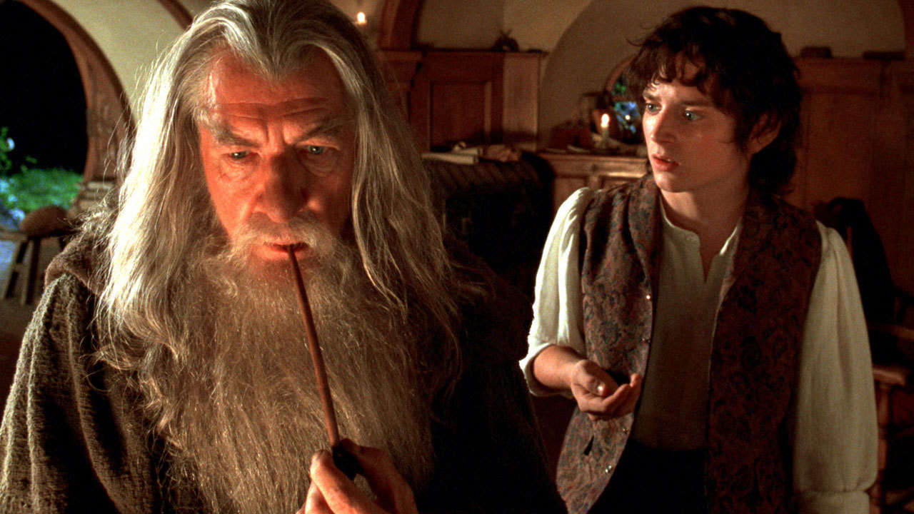 Gandalf (Sir Ian McKellen) stares into the distance while smoking a pipe and Frodo Baggins (Elijah Wood) stares intensely at Gandalf while in Bilbo's home.