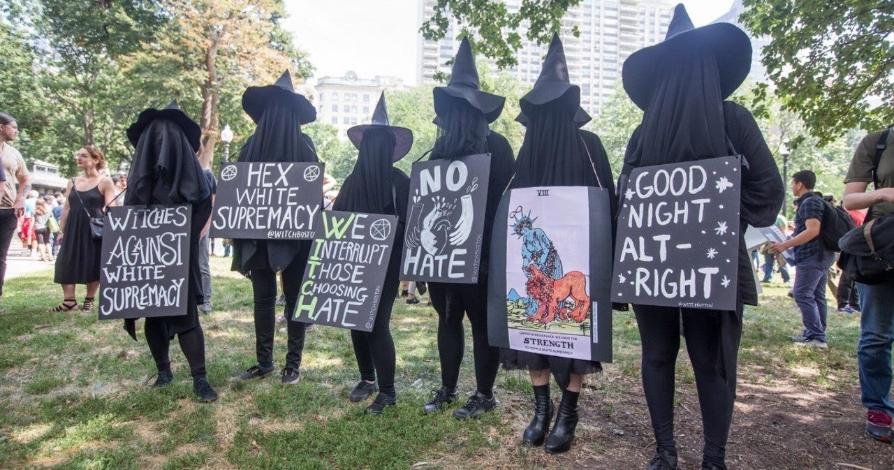 Proponents of WitchTok, a group of witches holding various signs with messages against white supremacy stand in a grassy field while attending a Black Lives Matter protest in Boston.