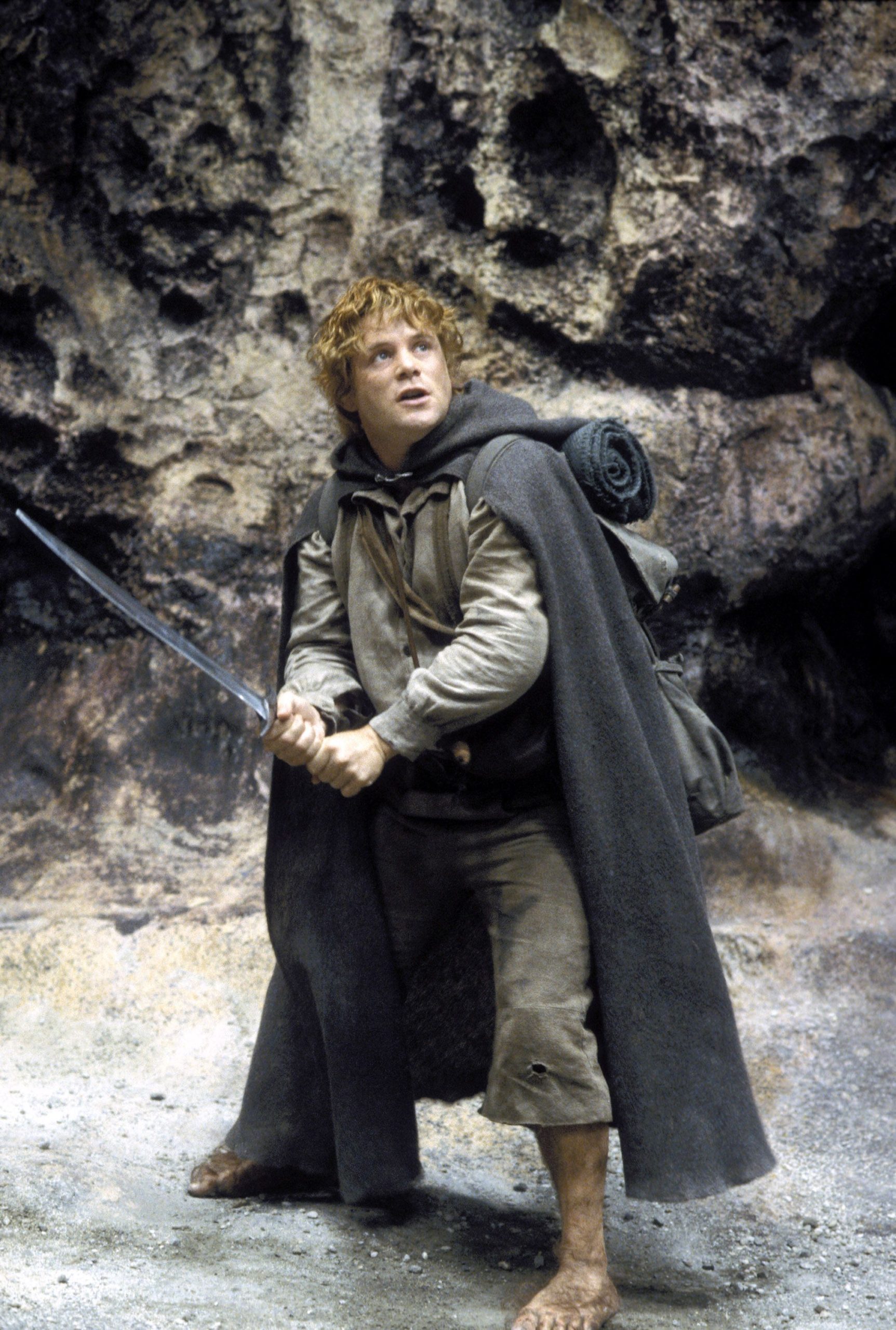 Samwise Gamgee (Sean Astin) wields a sword to defend himself and Frodo amidst a rocky slope.