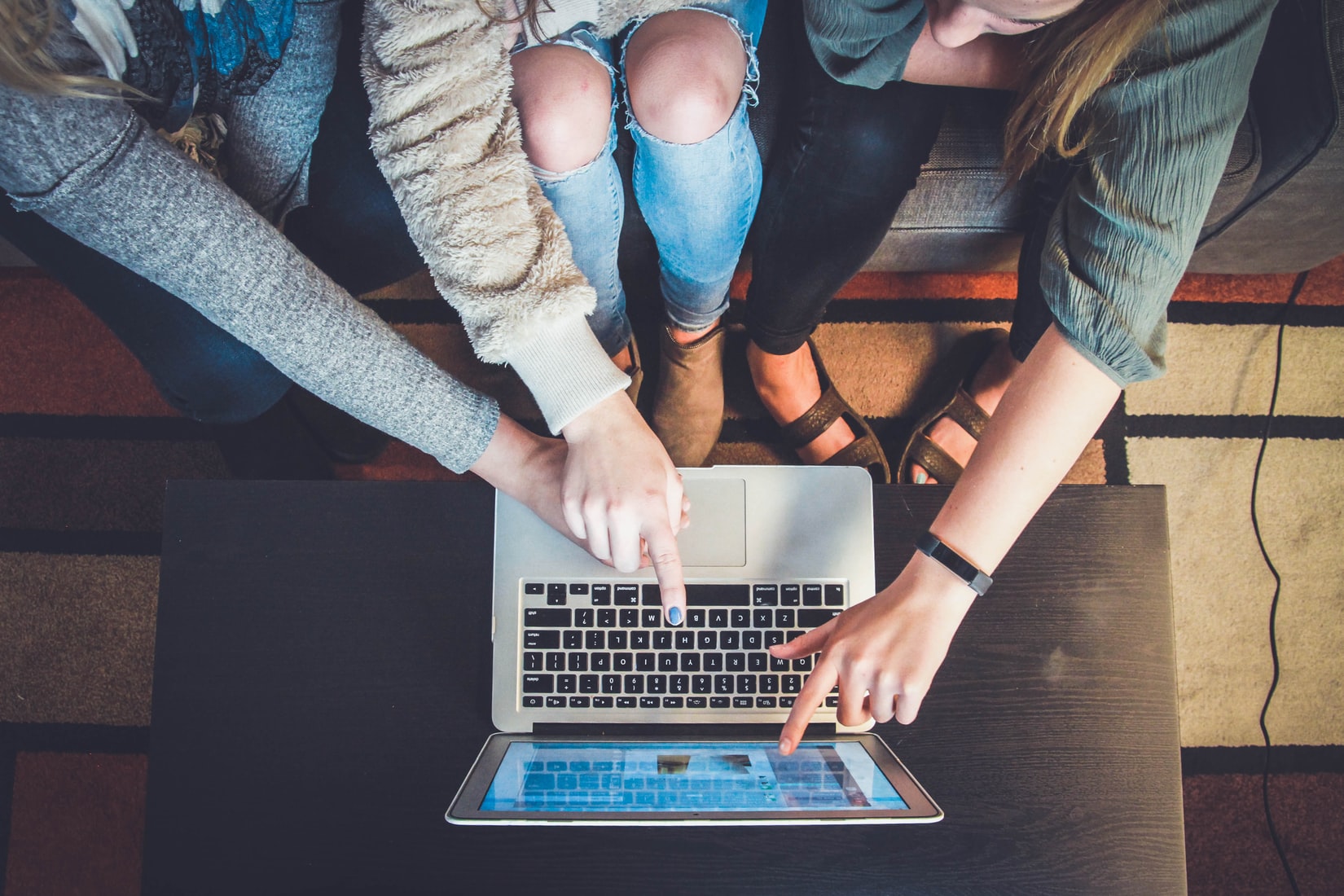 3 girls sit on a couch and point at a laptop screen. 