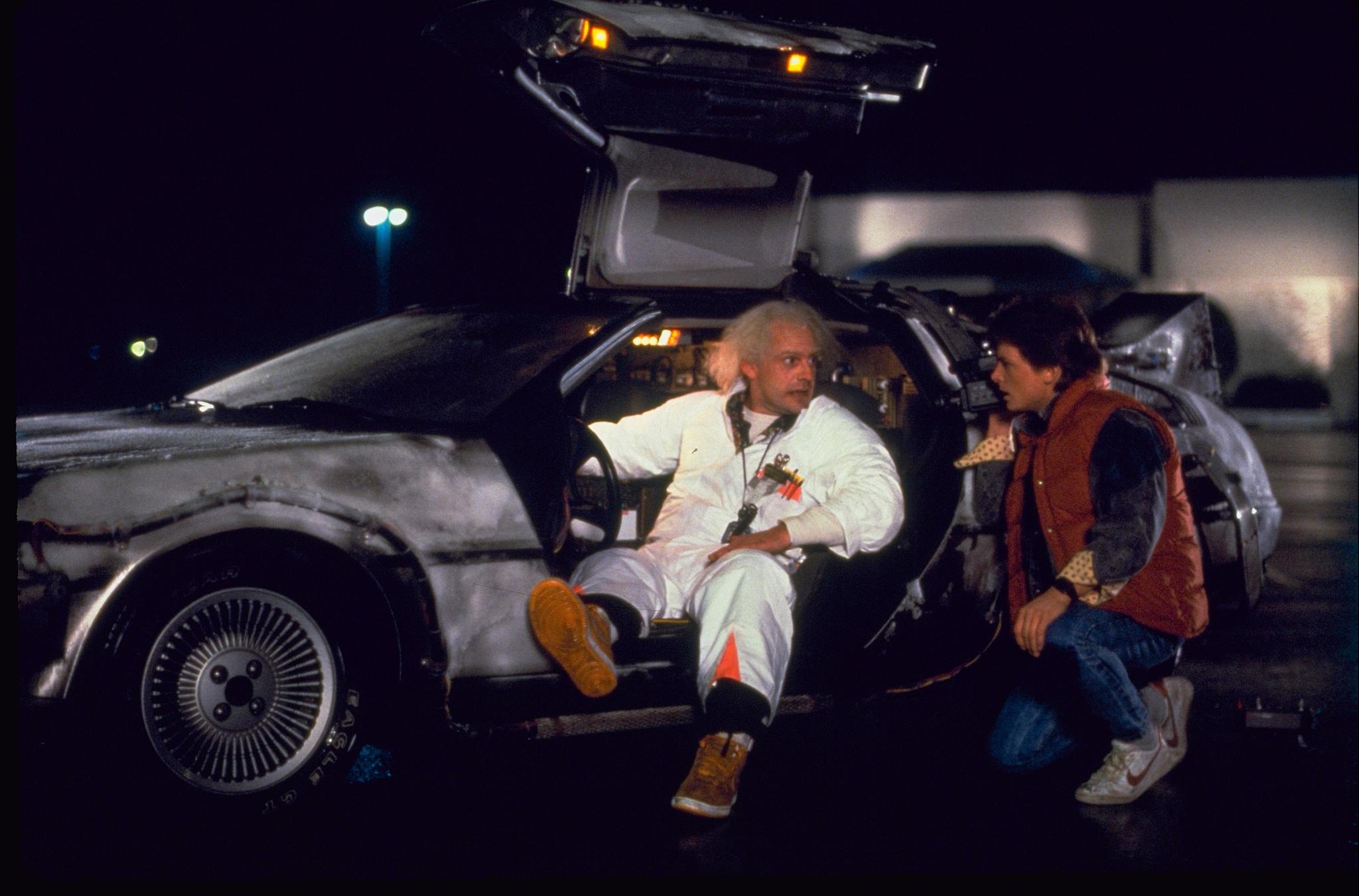 Image from Back to the Future of Doc Brown getting into the DeLorean and Marty McFly crouching next to him. 