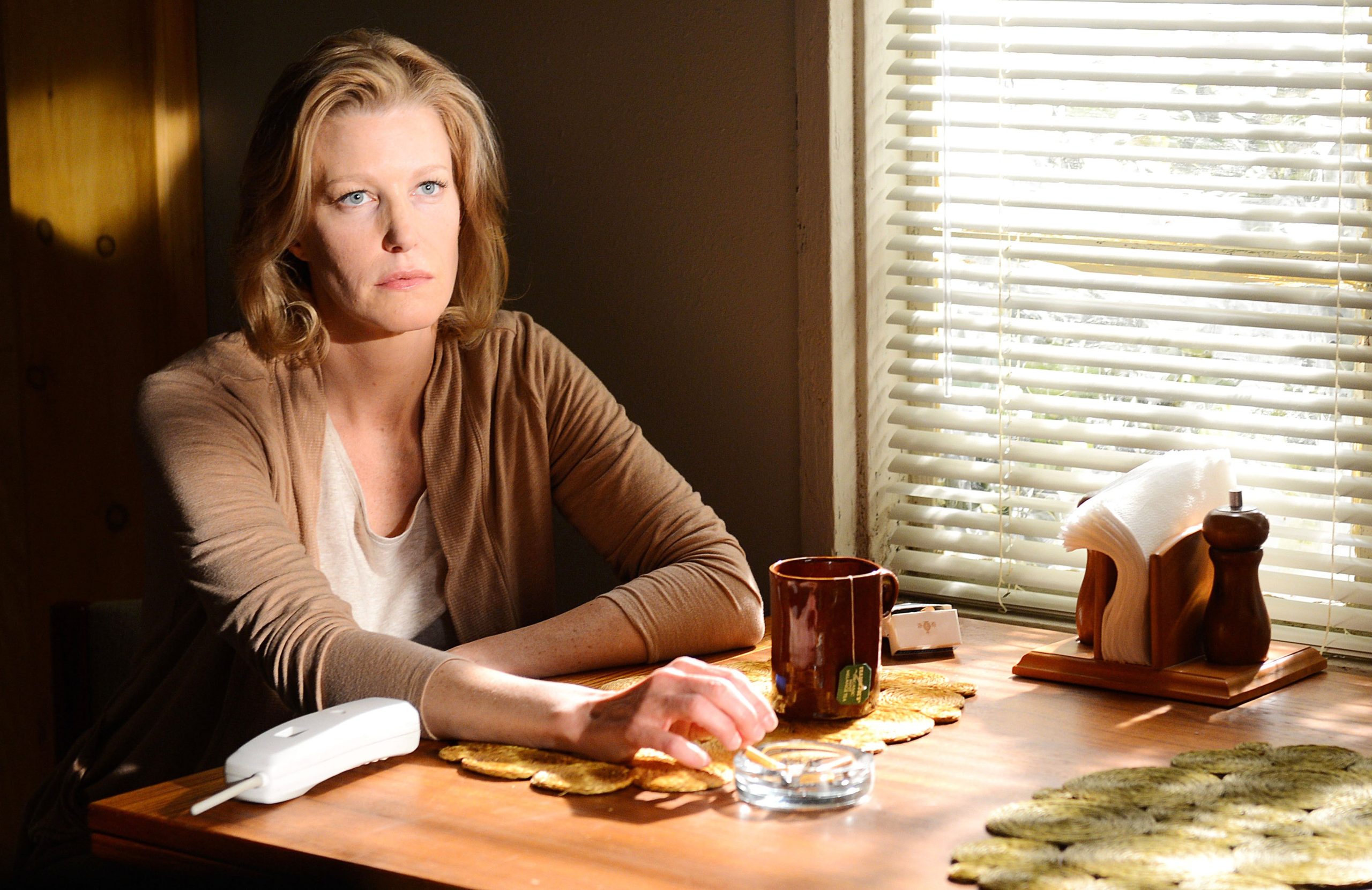 Skyler White from Breaking Bad sitting at her table, smoking a cigarette, and looking intensely at Walter White who is not in the frame.  