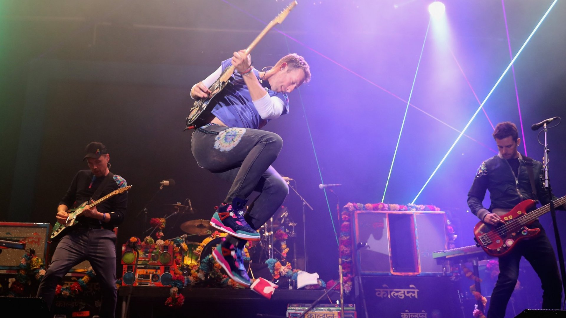 The members of Coldplay perform for their A Head Full of Dreams album.  Chris Martin is jumping while playing guitar.
