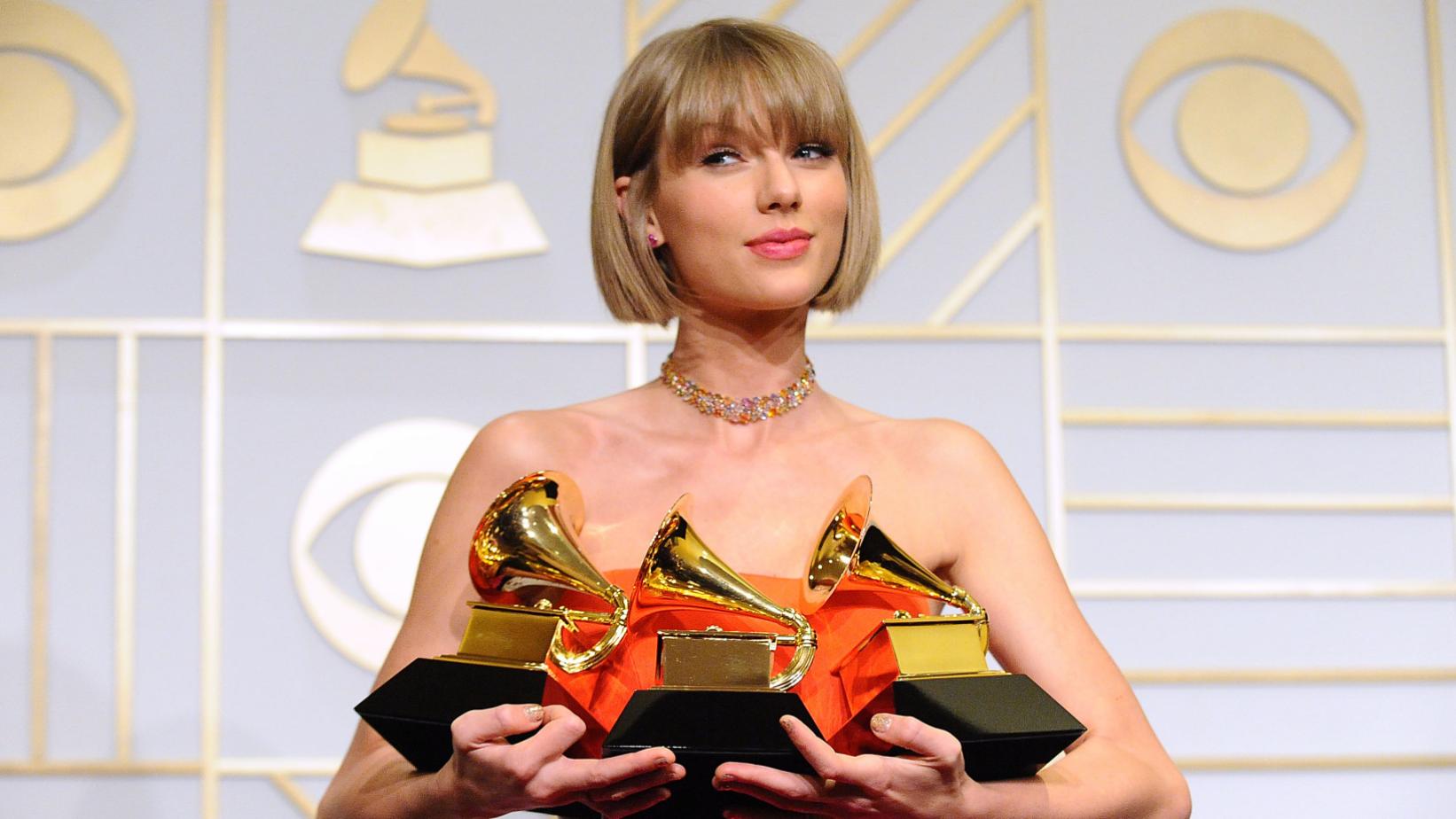 Popular Pop artist Taylor Swift on red carpet holding three awards