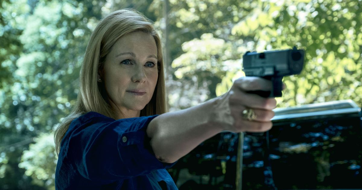 Wendy Byrde is pointing a gun at someone with an almost calm expression and slight smile.