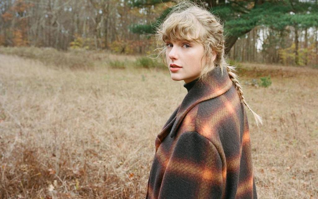 Taylor Swift with her hair in a braid, standing in a field looking back at the camera.