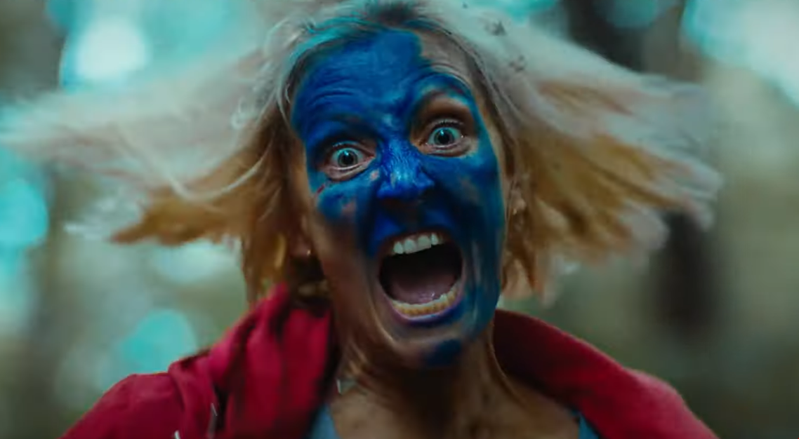 Eve runs towards the camera with blue paint on her face in the final scene of Hunted. Parannaud, Vincent, dir. Hunted. 2021.