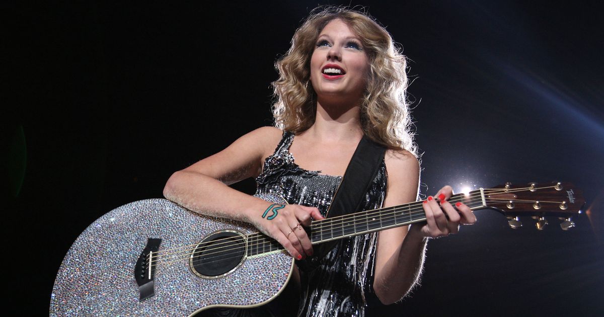 Taylor Swift on stage at her tour holding her sparkly guitar.