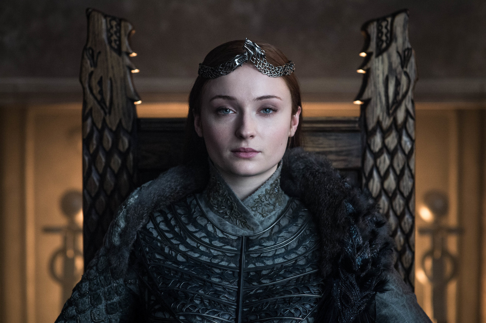 Sansa Stark, newly crowned Queen in the North, sits on the Stark throne with a crown on her head, staring down the camera.