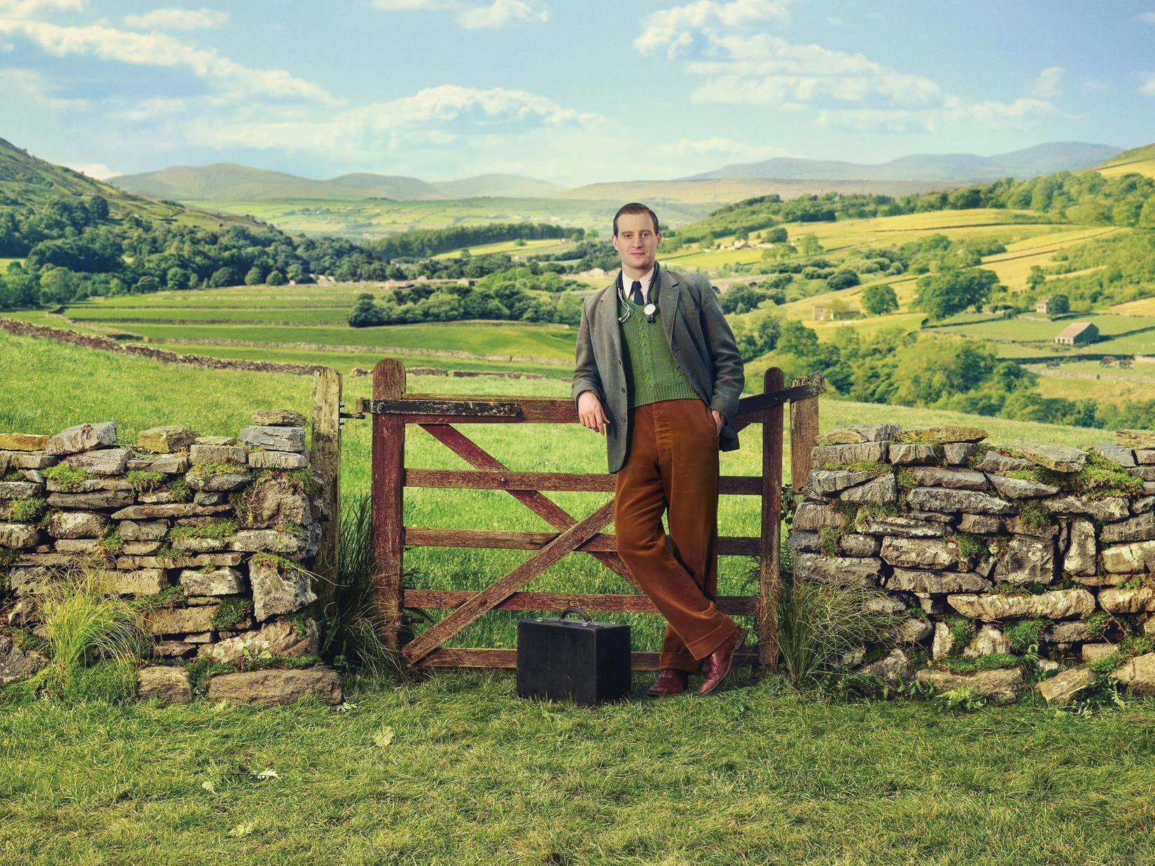 James Herriot stands by a fence in the verdant Yorkshire landscape in a promotional shot from All Creatures Great and Small, 2020. (Photo by Playground Entertainment/PBS).