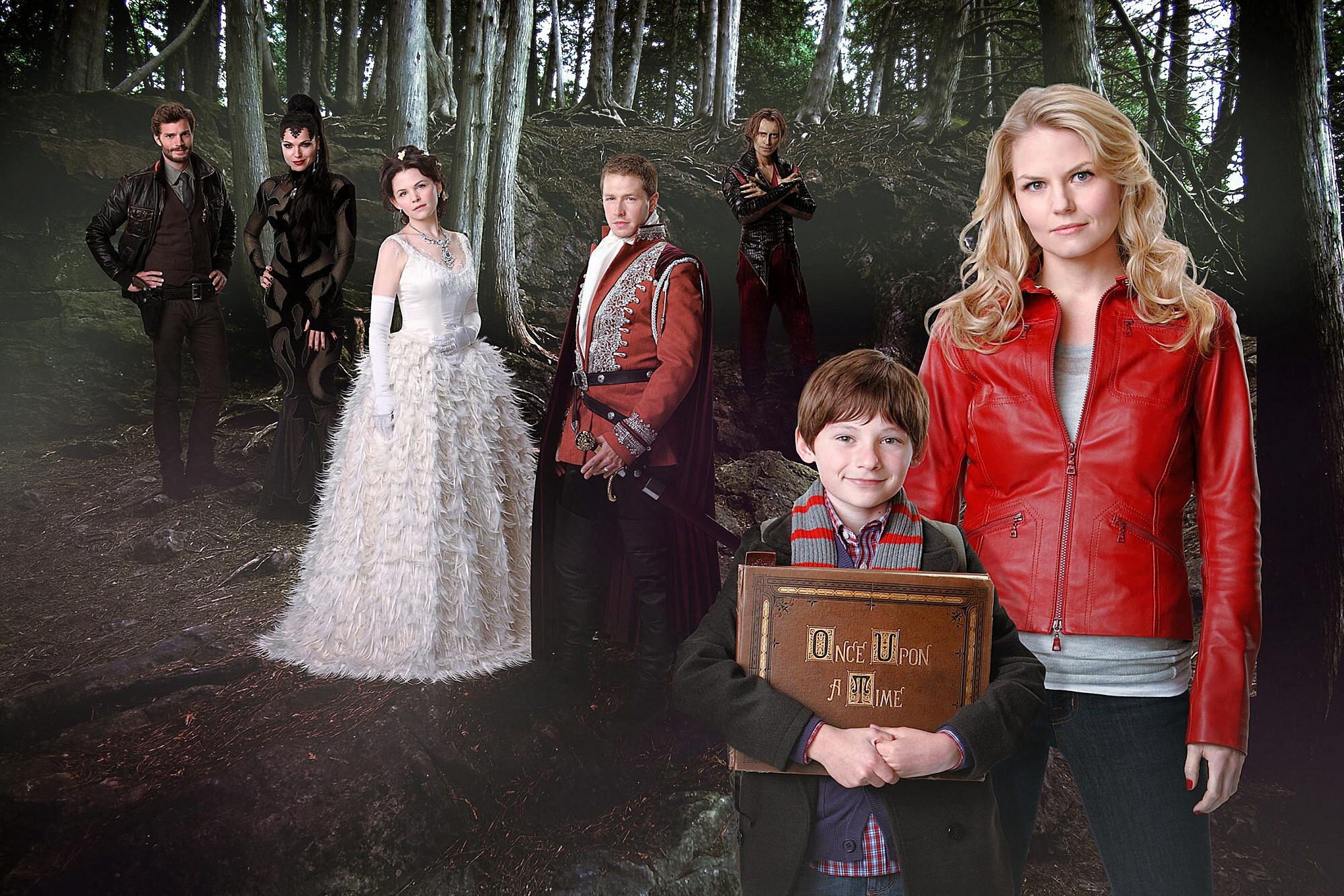 Once Upon a Time's original cast, Emma, Henry, Regina, Snow, David, Rumplestiltskin, and Graham, are posing for the camera in the enchanted forest.