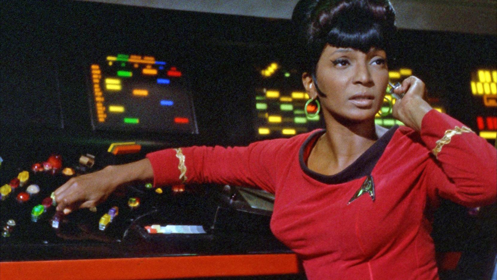 Nyota Uhara, played by Nichelle Nichols in the first generation of Star Trek. Uhara sits at her desk at the USS Enterprise, with a look of determination. 
Star Trek. 1966-1969. NBC.