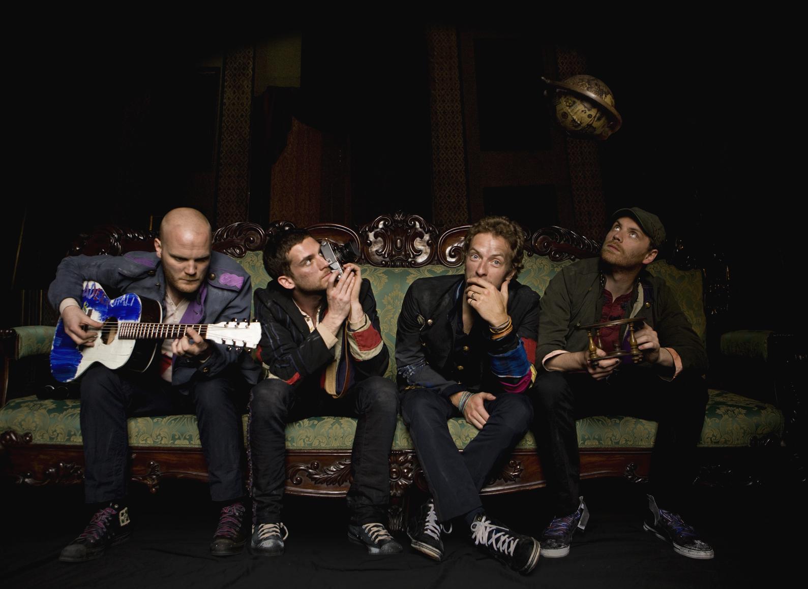 Will Champion, Guy Berryman, Chris Martin, and Jonny Buckland sit on a couch in the costumes associated with their "Viva la Vida" album.  Only Chris Martin looks at the camera.