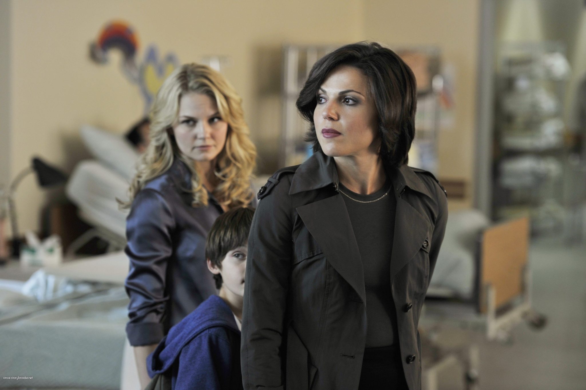 Regina, Emma, and Henry are starring into a hospital room where an unseen Charming is resting.
