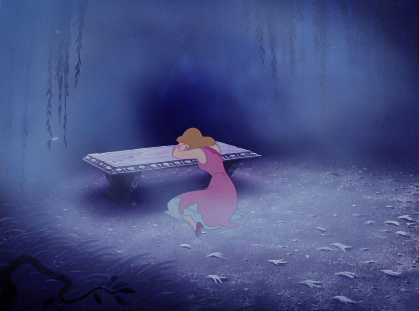 Cinderella is laying her head on her arms and crying over a bench outside over her torn, pink dress.